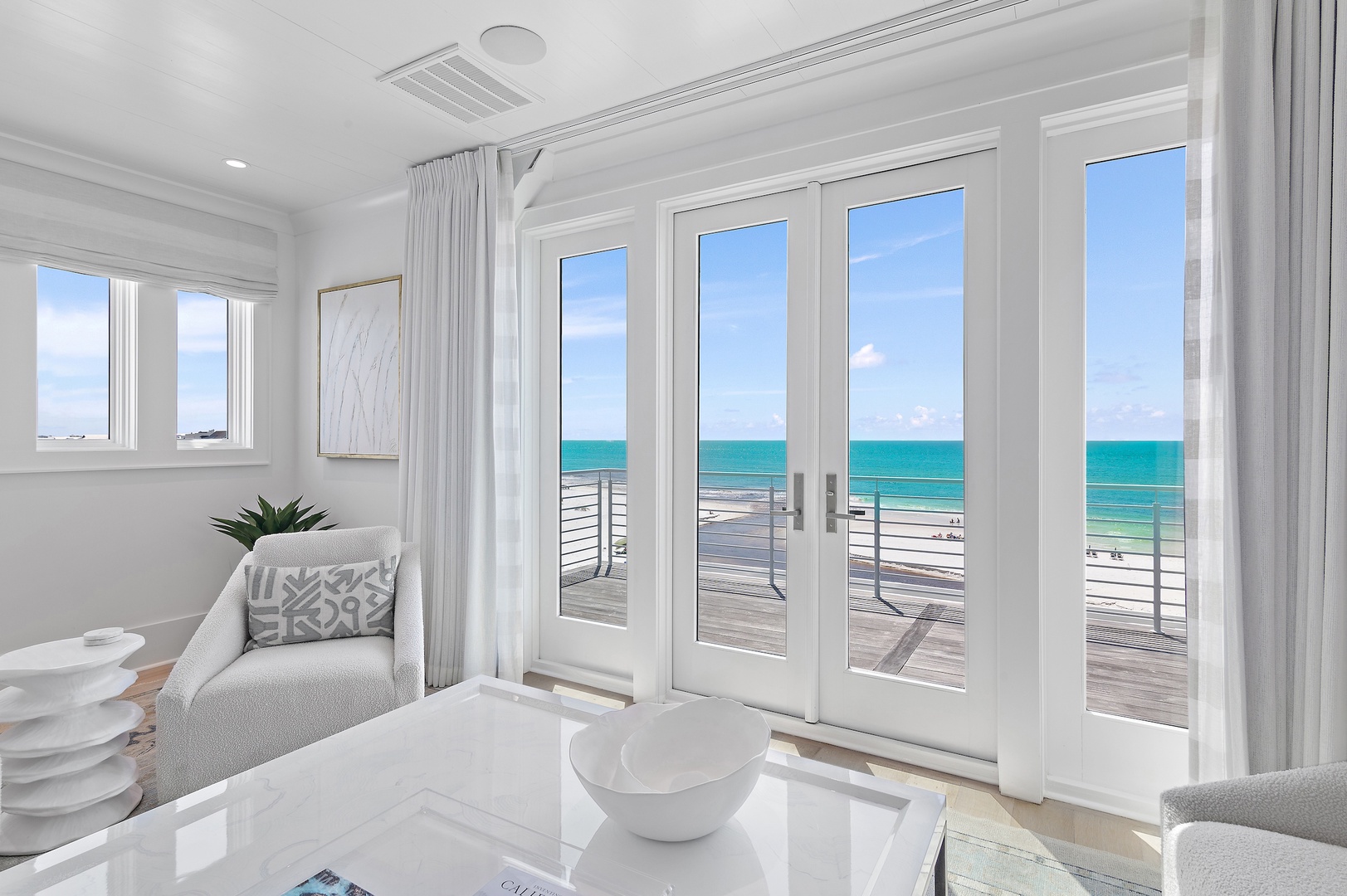 Picture yourself relaxing in this serene coastal living space, where floor-to-ceiling glass doors frame an endless turquoise horizon. Your private balcony beckons, offering unobstructed ocean views and the soothing sound of waves just steps away.