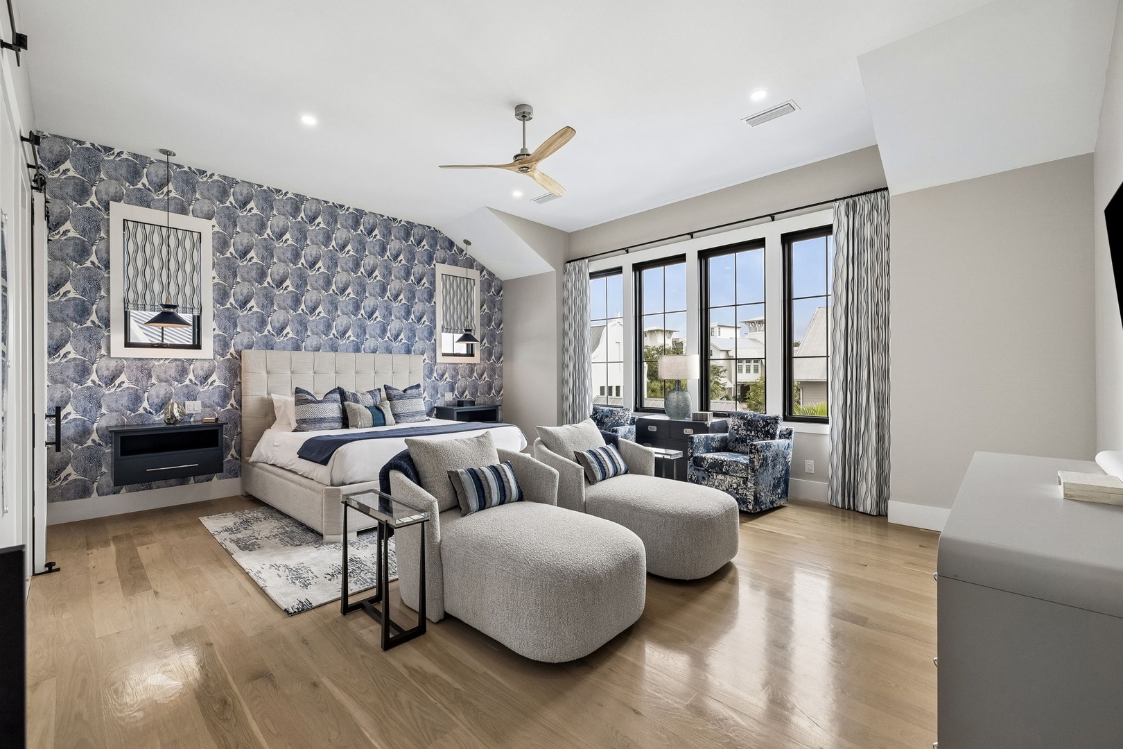 Sink into your spacious bedroom with elegant touches: a bold accent wall, cozy lounge seating, and sunlight streaming through expansive windows. Your private retreat awaits.