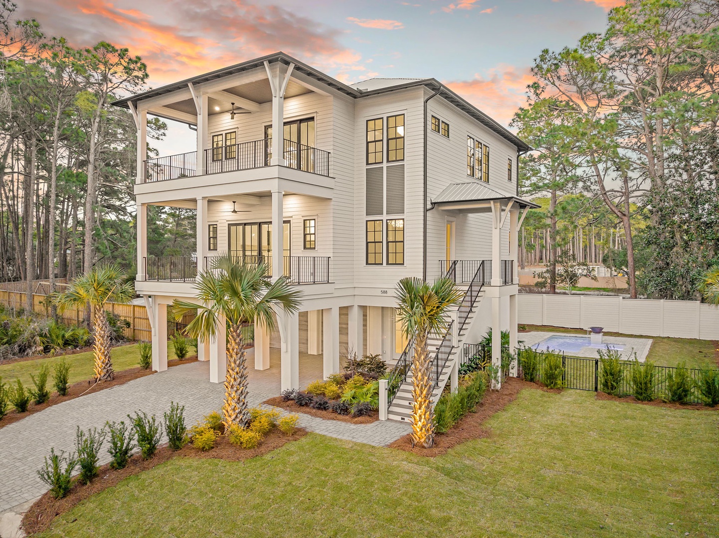 Modern three-story coastal home with multiple covered balconies, surrounded by palm trees and mature landscaping in a peaceful wooded setting.