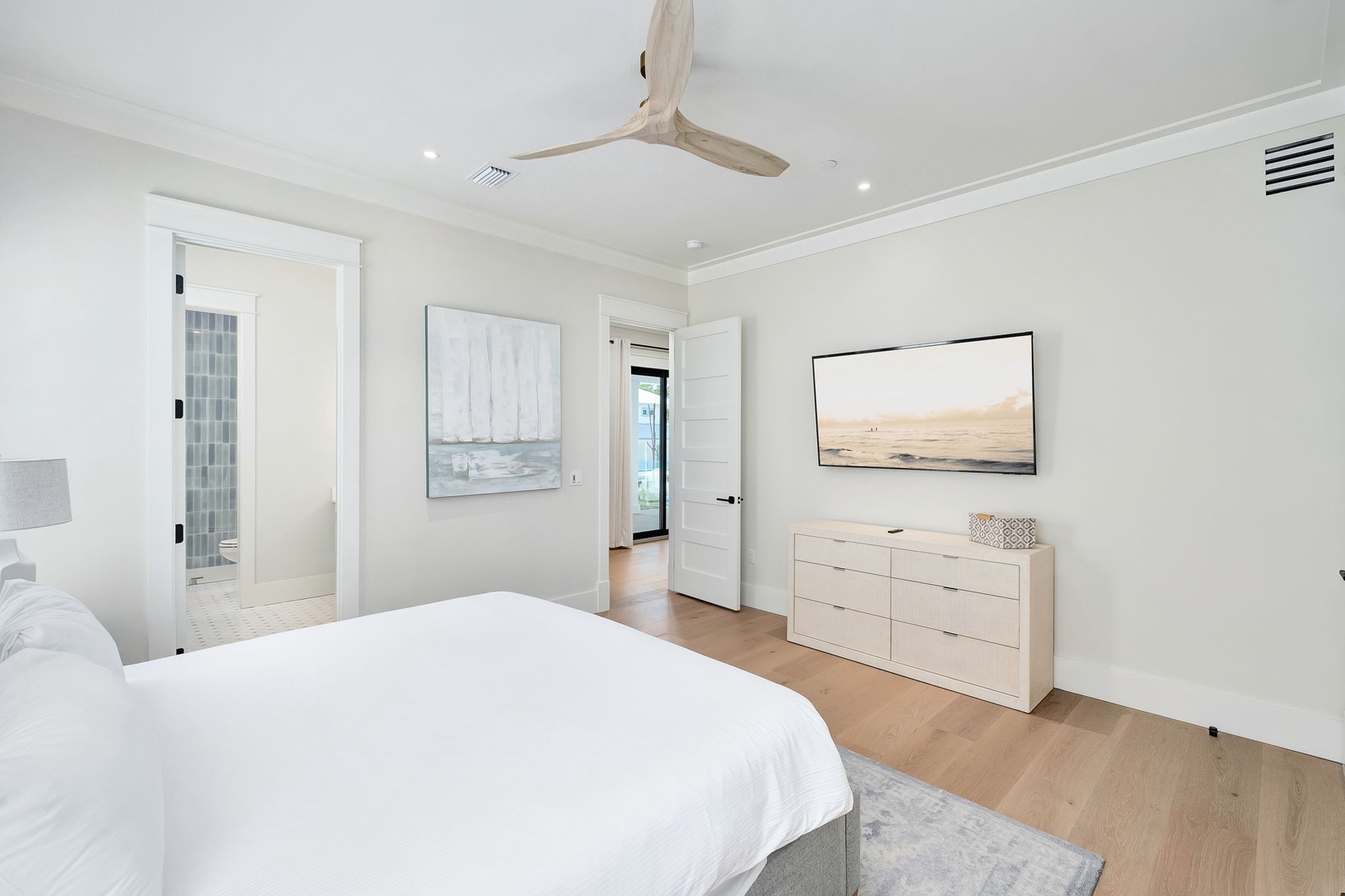 Your serene coastal retreat awaits in this bright bedroom, where crisp linens and soft neutrals create a calming sanctuary. A gentle ceiling fan whispers above while you drift off to sleep.