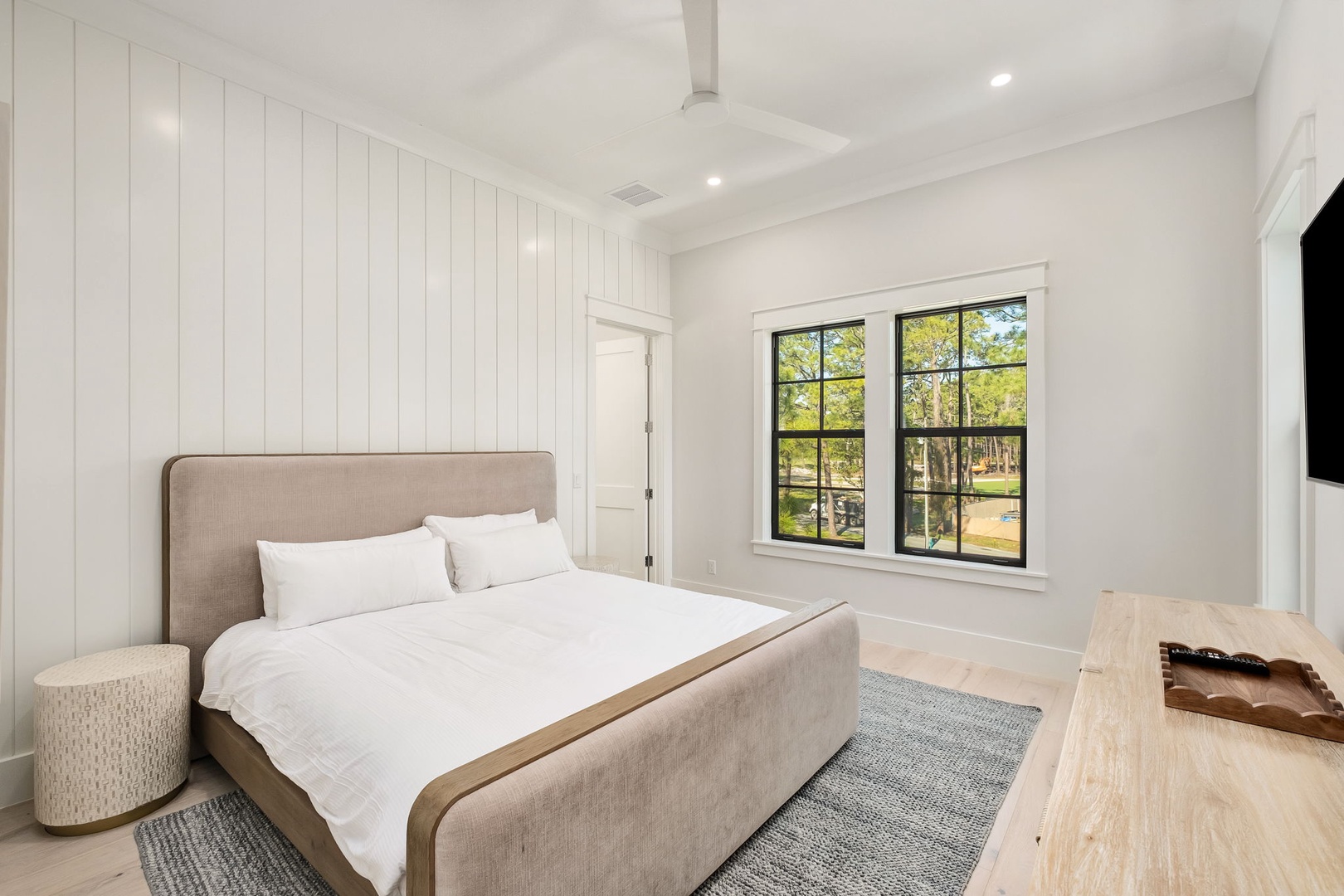Wake up refreshed in your bright, airy bedroom featuring crisp white linens and peaceful garden views through oversized windows.
