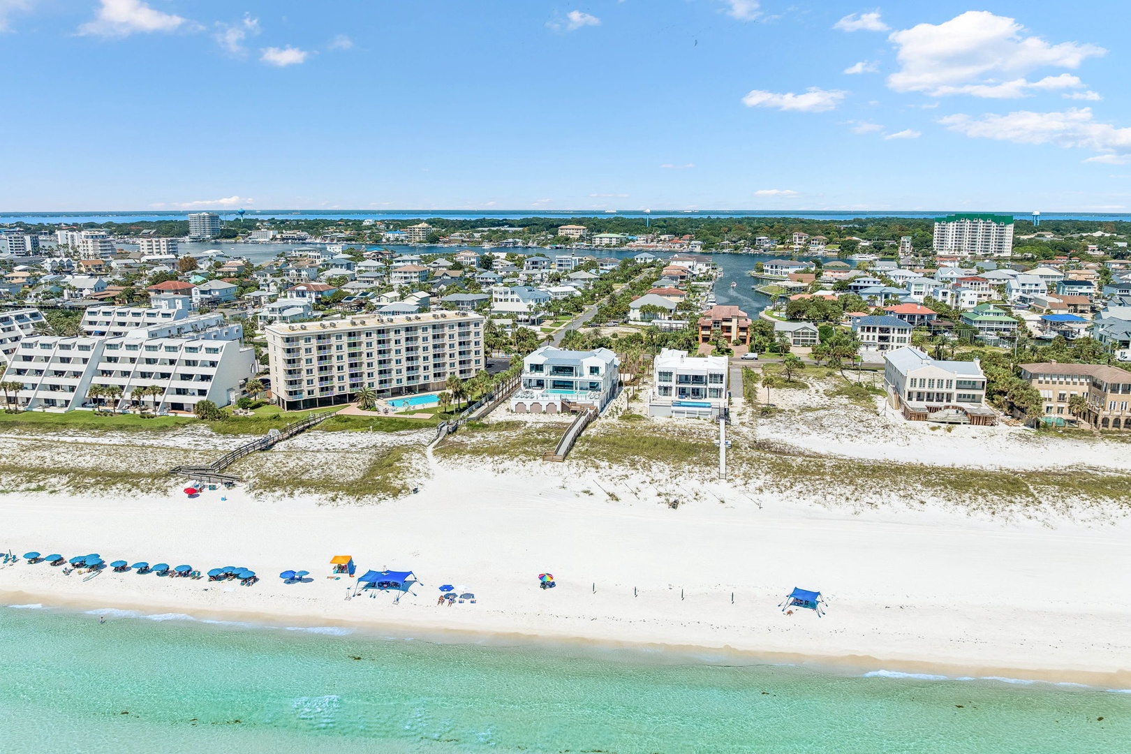 Aerial view of a pristine beachfront community with white sand shores, turquoise waters, and coastal residential properties nestled between the Gulf and inland waterways.