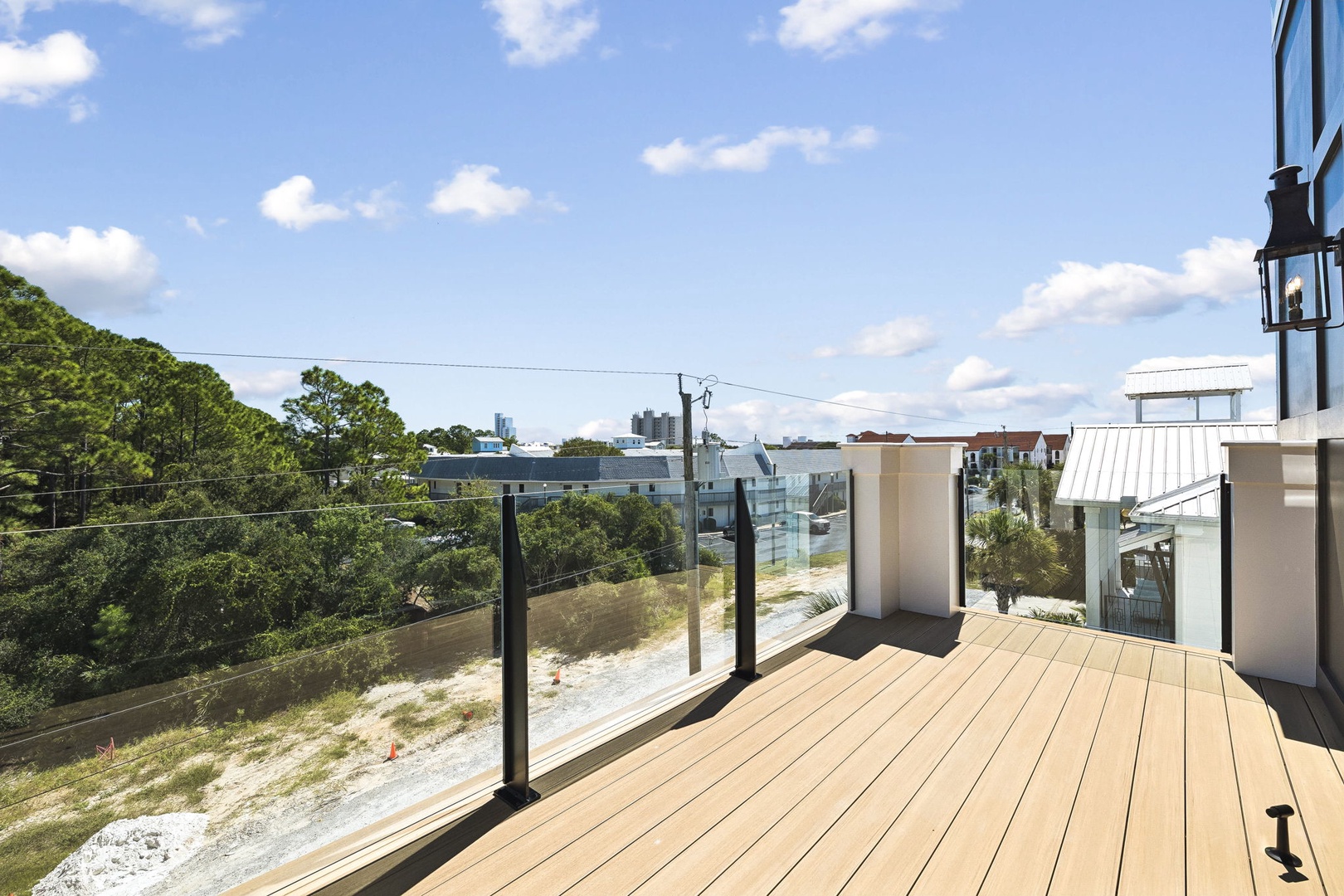 A spacious private deck with sleek glass railings showcases the surrounding neighborhood and treetops. Imagine morning coffee under open skies, with fresh air and a peaceful coastal vibe just for you.