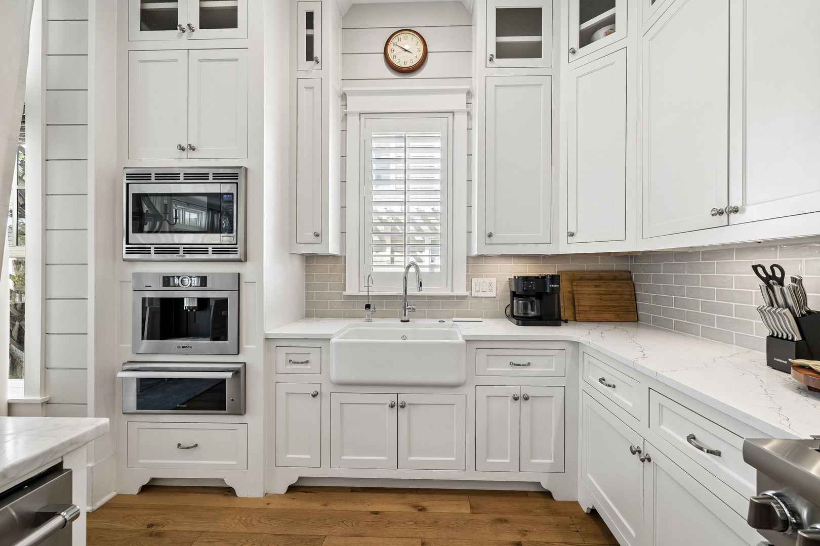 Your vacation home kitchen blends classic elegance with modern convenience, featuring a farmhouse sink, marble-look countertops, and built-in appliances—everything you need to prepare meals in comfort and style.