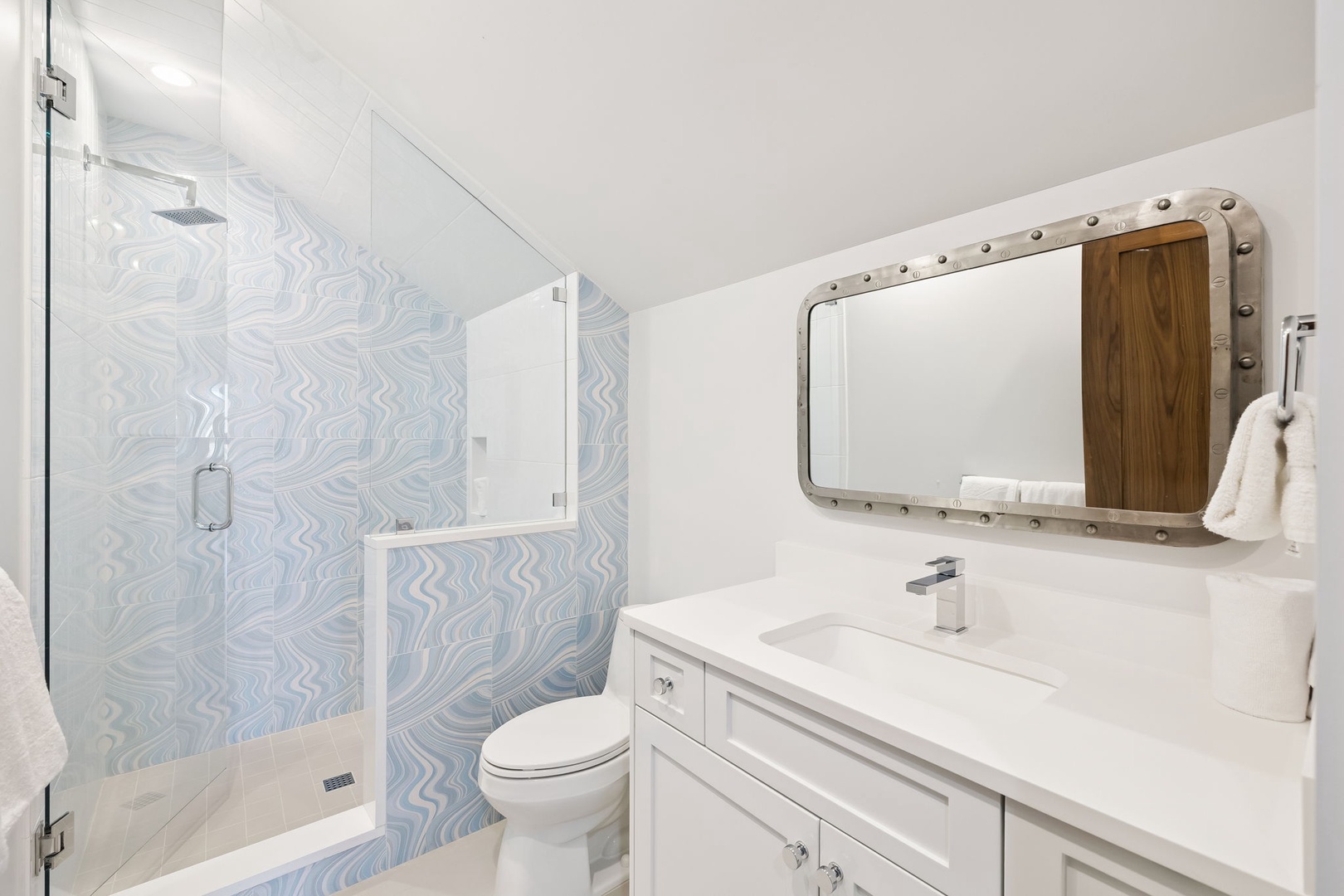 Refresh in your stylish bathroom featuring a spacious walk-in shower, modern vanity, and unique wave-pattern tiles that create a serene spa-like atmosphere.