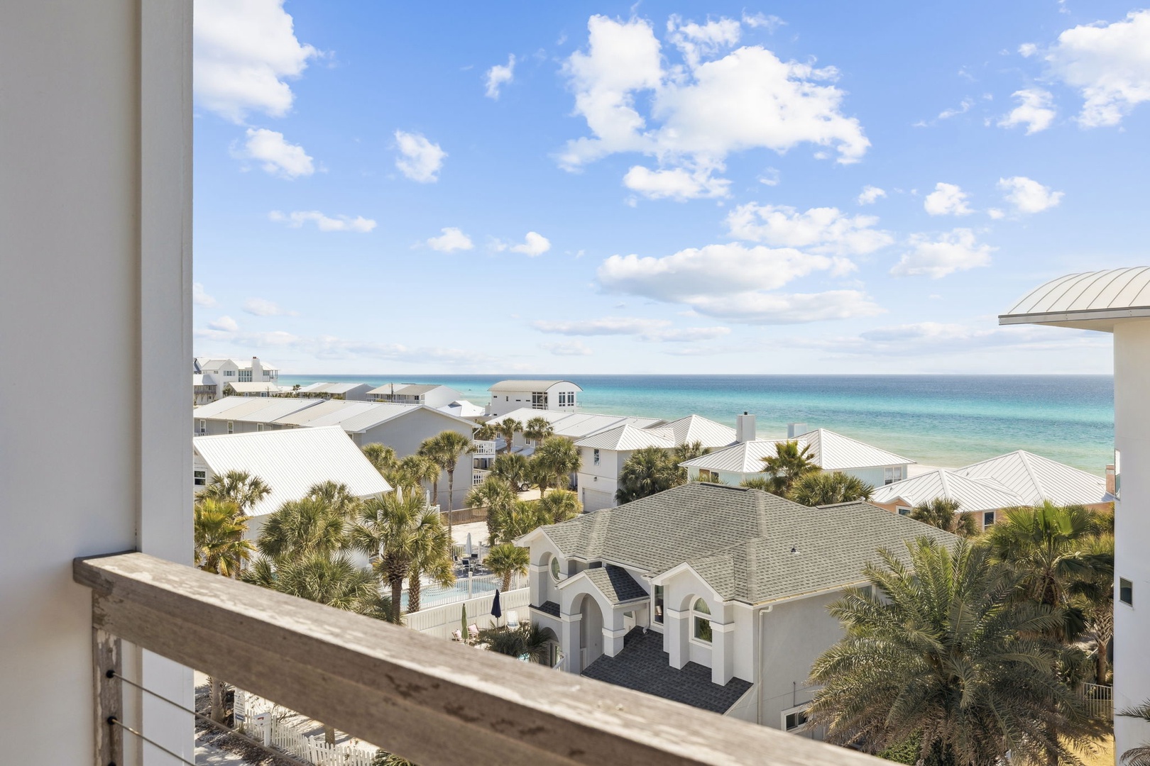 Panoramic coastal view showcasing pristine turquoise waters and charming beachside community with palm trees and white-roofed homes.
