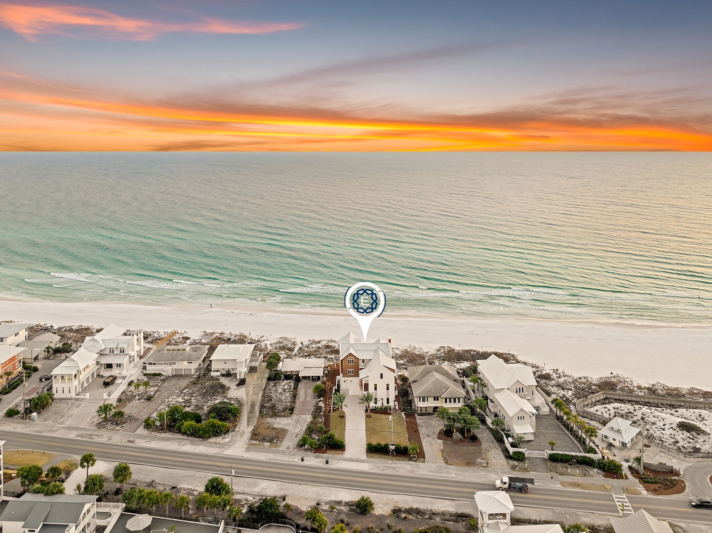 Stunning aerial view showcases beachfront properties along pristine white sand and emerald waters during golden hour.