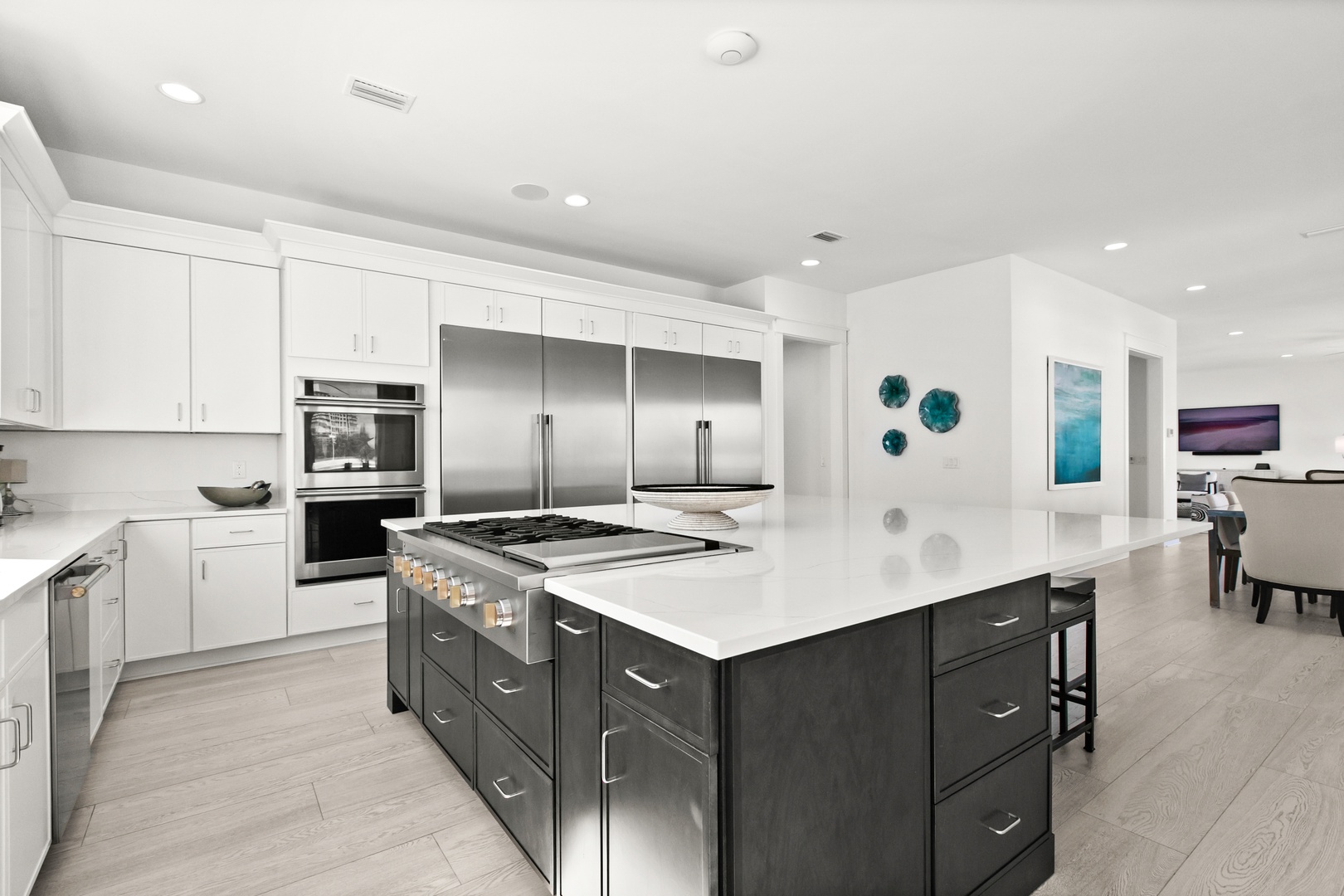 Your sleek chef's kitchen awaits with professional-grade appliances, a spacious island with gas cooktop, and elegant white cabinetry flowing into the bright, open living area.