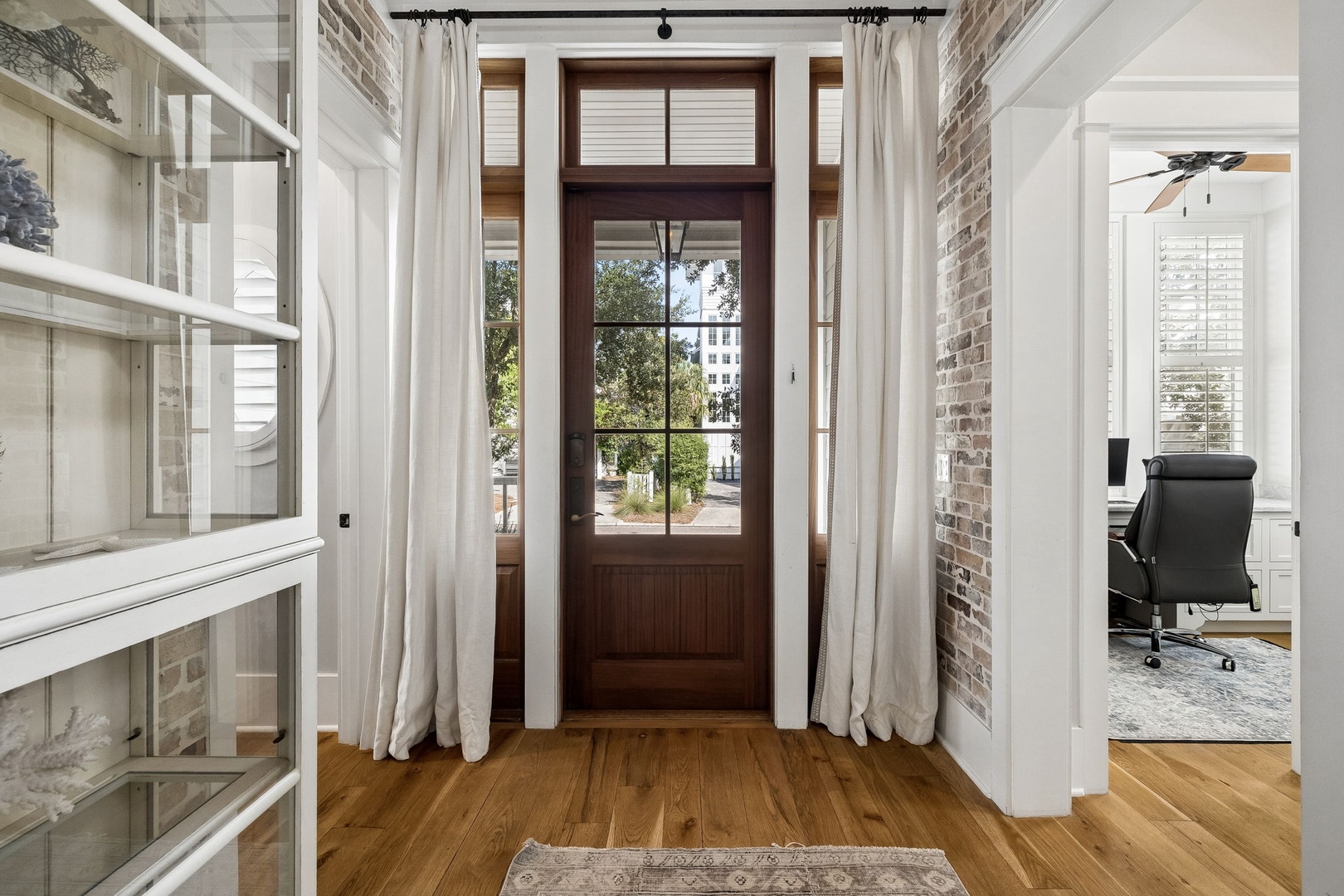 A bright entryway with exposed brick walls, warm wood floors, and a welcoming glass-paneled door. Natural light streams through, creating an inviting first impression as you arrive.