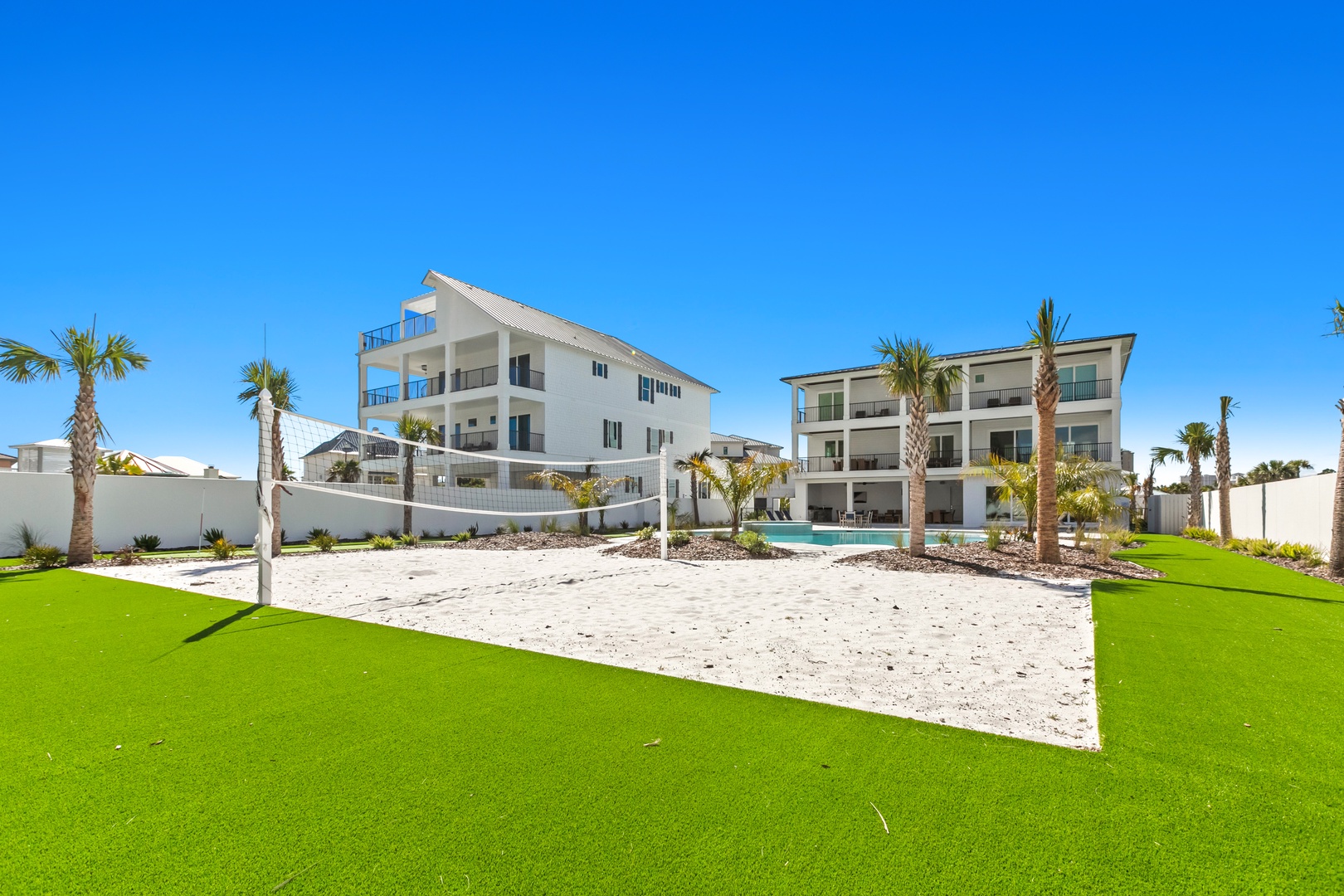 Modern beachfront buildings with lush landscaping, palm trees, and pristine white sand under a brilliant blue sky.