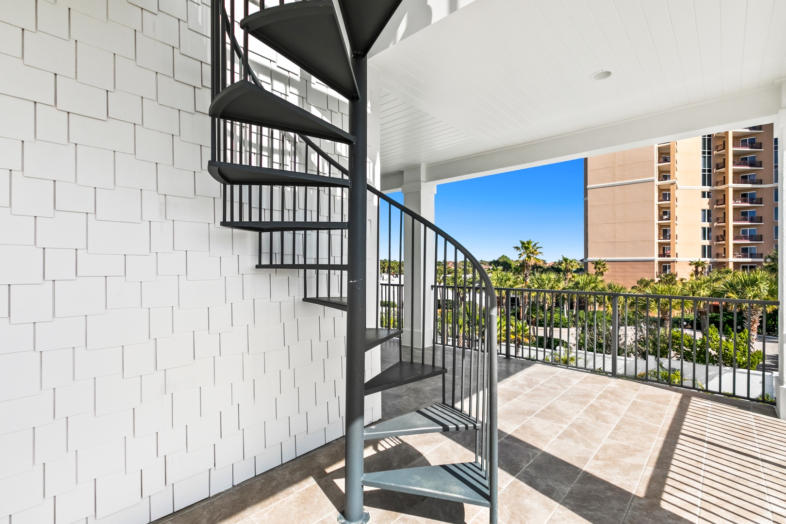 Step outside to your private balcony with a stylish spiral staircase, where palm trees sway and neighboring buildings frame a bright, sunny day. A perfect spot for morning coffee or unwinding with a view.