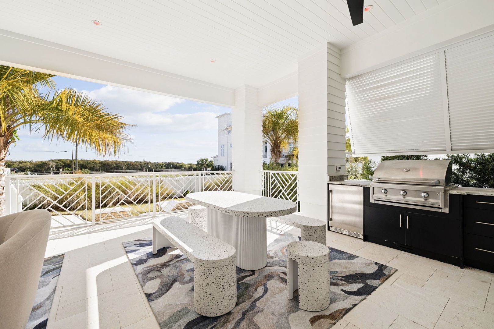 Your covered terrace features a stylish dining setup and full outdoor kitchen, perfect for alfresco meals with tropical palm views.