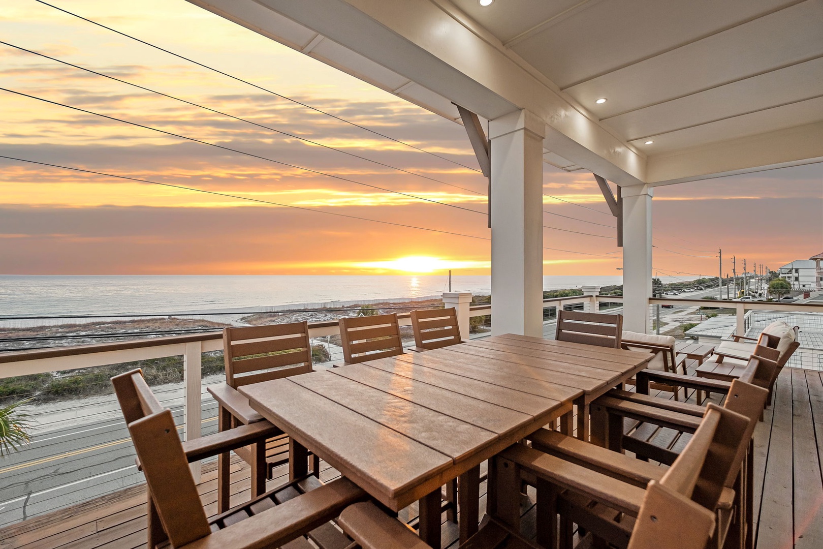 Stunning oceanfront deck overlooking sandy beach and marina with dramatic sunset views.