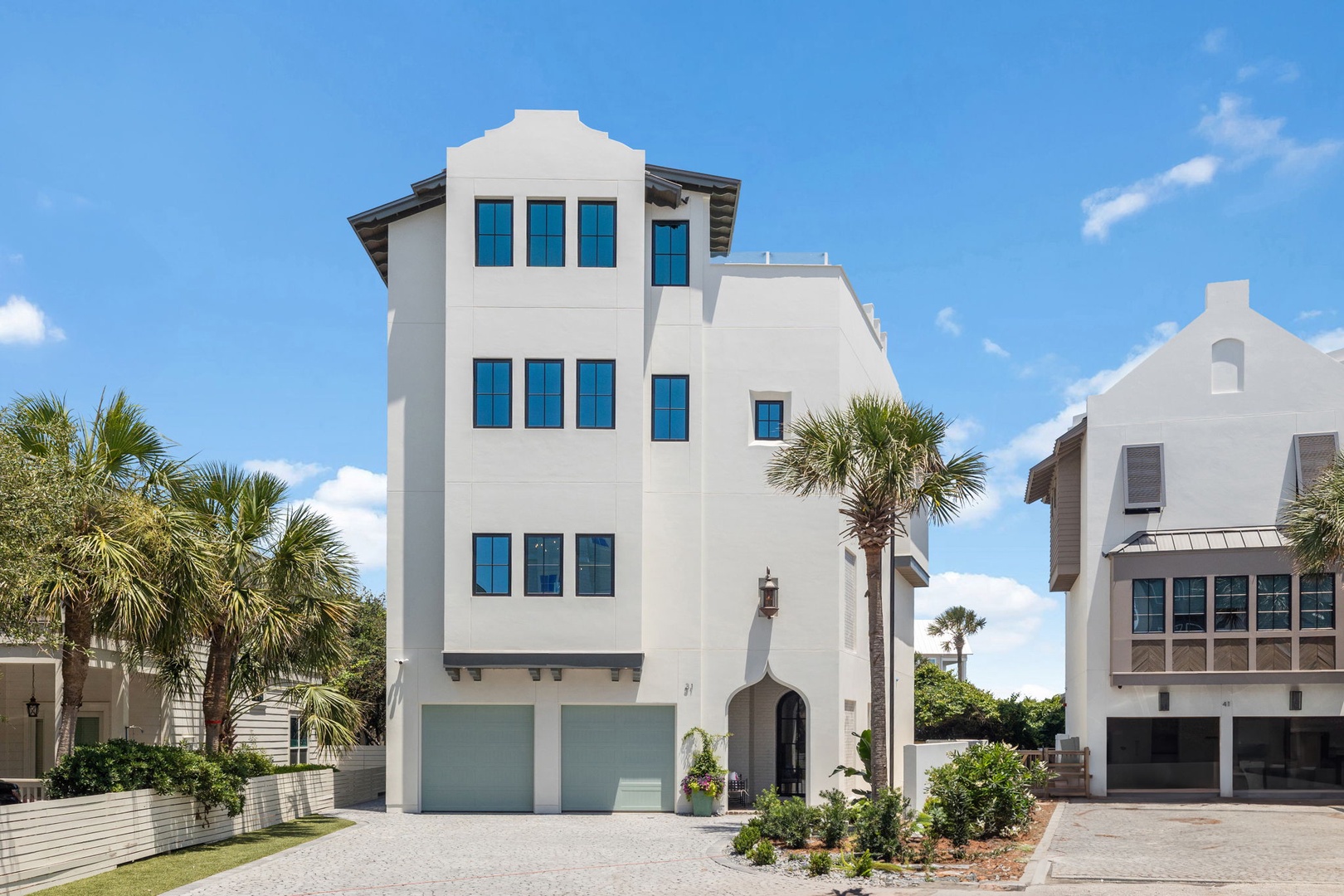 This striking multi-level property features Mediterranean-inspired architecture with a distinctive tower design, framed by tropical palms and neighboring coastal homes.