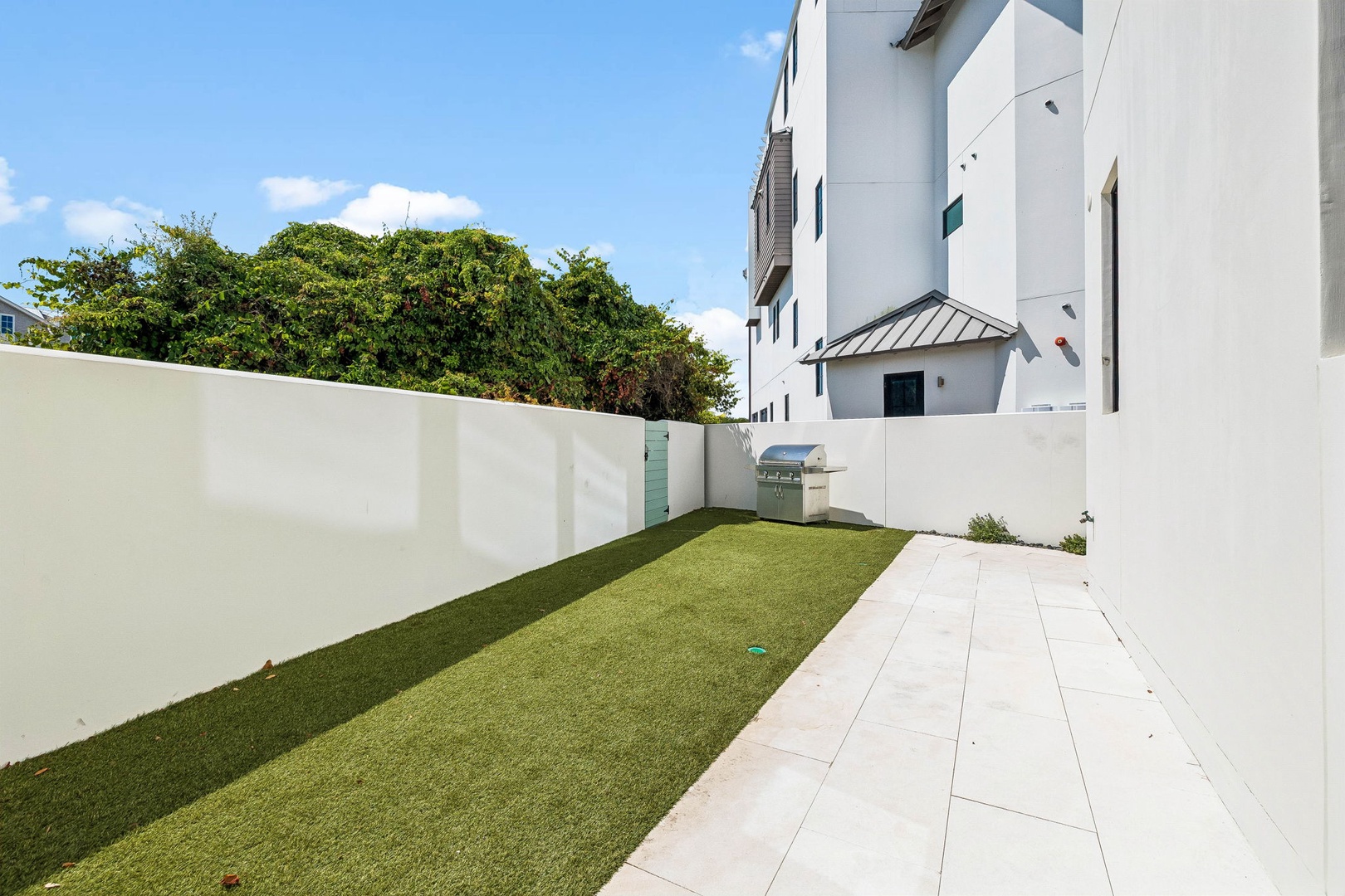A modern, private outdoor retreat featuring lush green lawn and contemporary patio—perfect for morning coffee, outdoor dining, or simply soaking up the sunshine. Built-in BBQ grill ready for your next cookout.