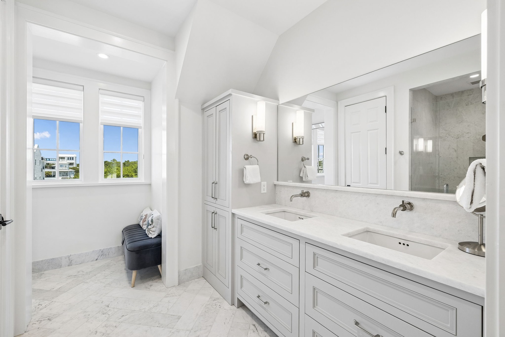 Refresh and unwind in this pristine, spa-like bathroom with dual vanities, elegant marble counters, and a cozy seating nook bathed in natural light from your window view.
