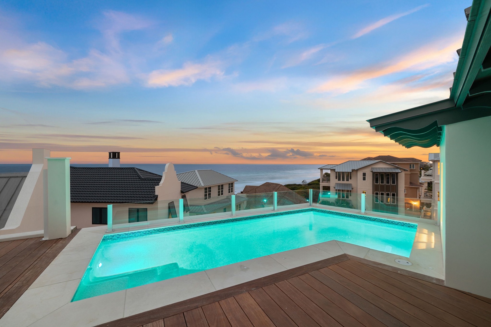 Private rooftop pool overlooking coastal homes and ocean at dusk, framed by soft sunset hues and gentle sea breezes in an exclusive residential neighborhood.