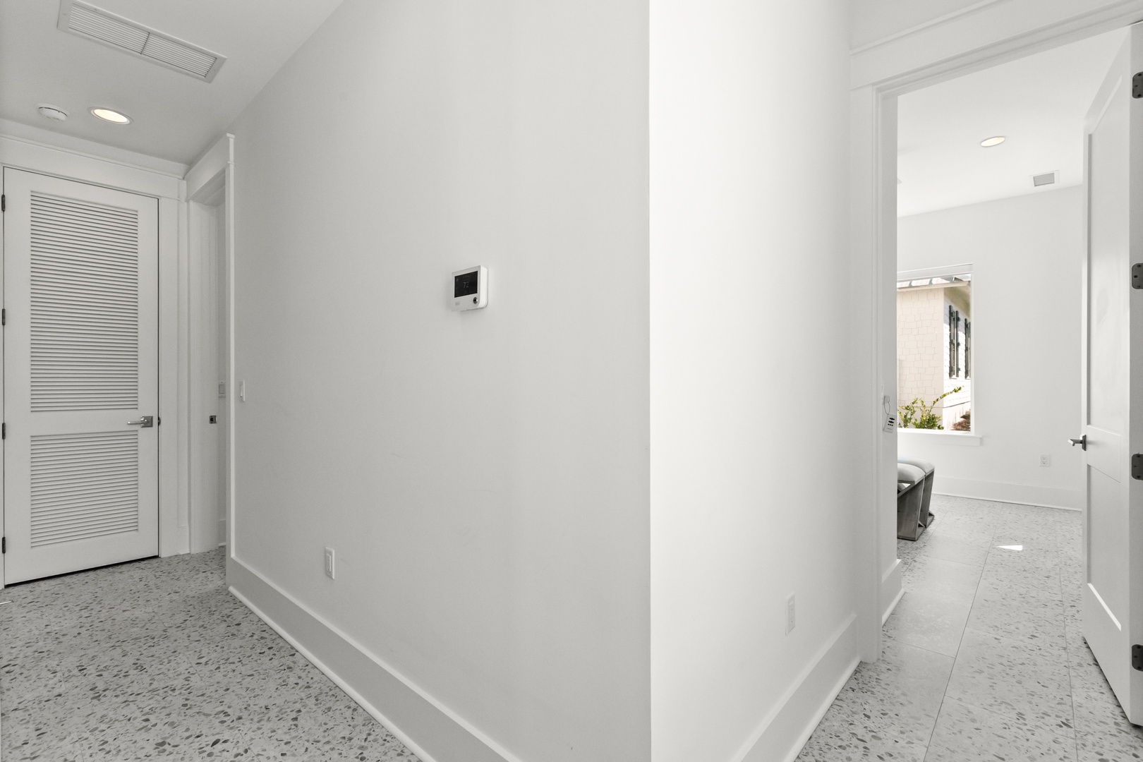 Step into your bright hallway with modern terrazzo floors and sleek climate control, where crisp white walls and natural light guide you to restful bedrooms just beyond.