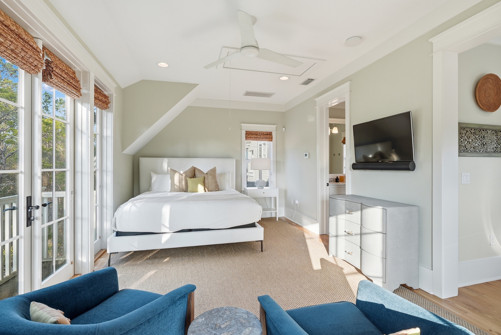 Relax in your serene bedroom suite with plush bedding, a private balcony, and stylish seating where sunlight streams through French doors, inviting peaceful mornings and restful evenings.