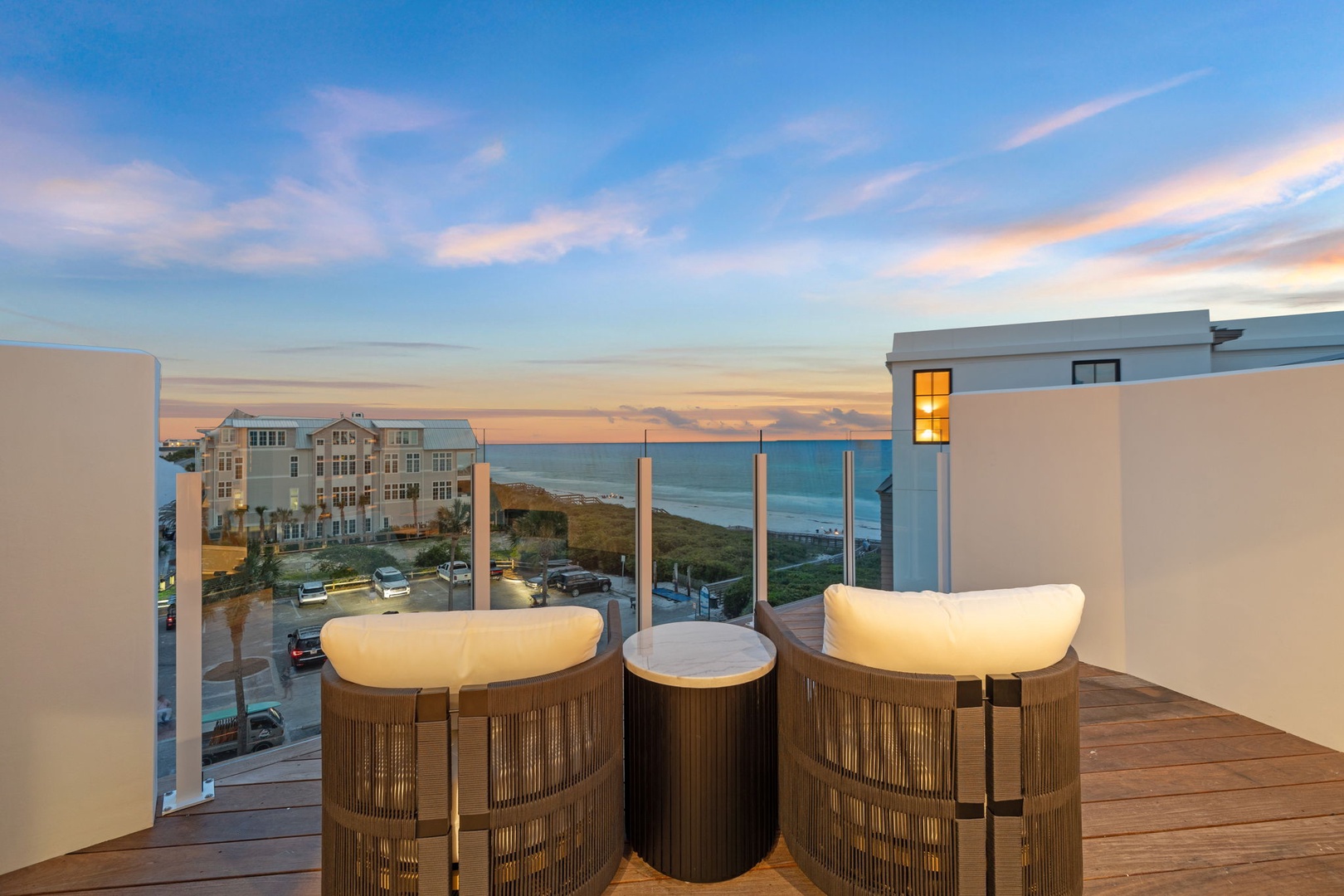 A rooftop balcony frames stunning ocean views at dusk, offering modern seating and a tranquil coastal backdrop for the property's beachside location.