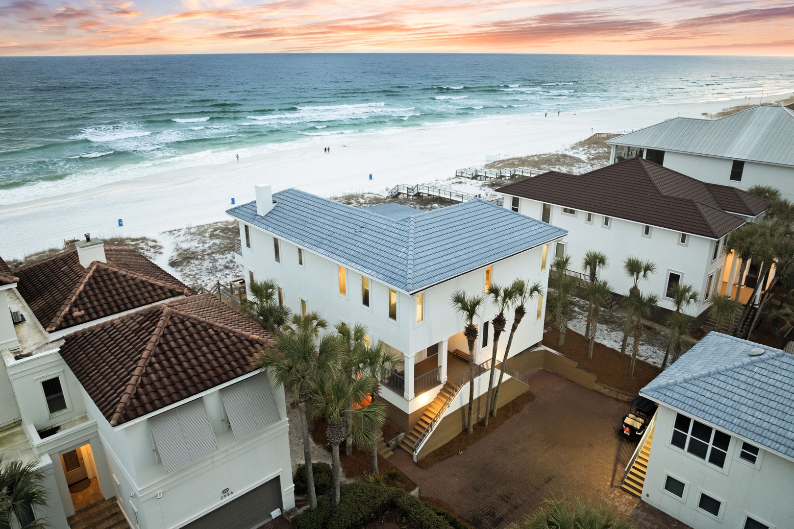 Beachfront vacation homes showcase stunning white sand beaches and emerald waters during golden hour sunset.