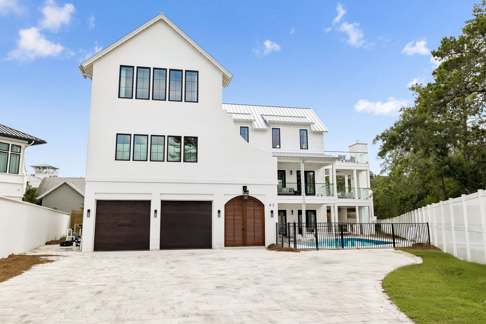 Modern coastal property featuring clean white exterior, metal roof, spacious balconies, and private pool area, set in a peaceful residential neighborhood with mature trees.