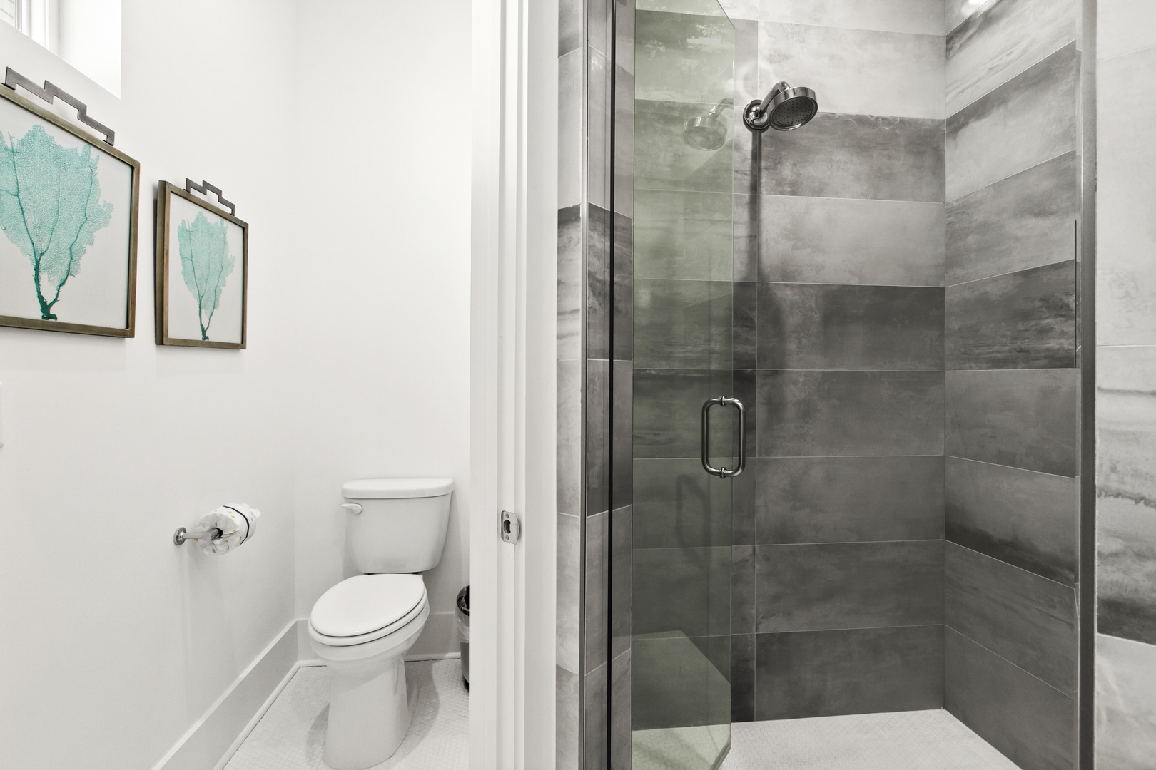 Step into your private bathroom with a sleek walk-in shower, modern gray tile, and calming coastal artwork to set the mood for your getaway.