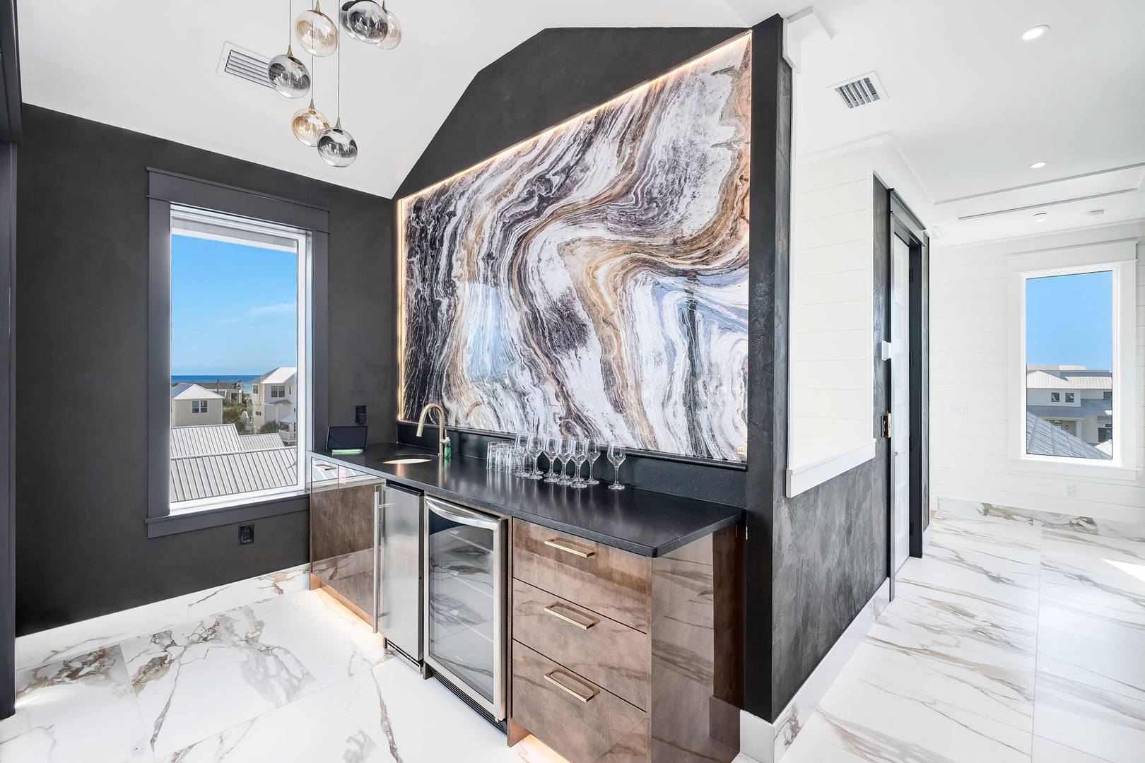 Your private wet bar features stunning marble floors, modern pendant lighting, and an artistic statement wall, perfect for mixing cocktails while enjoying ocean glimpses through dual windows.