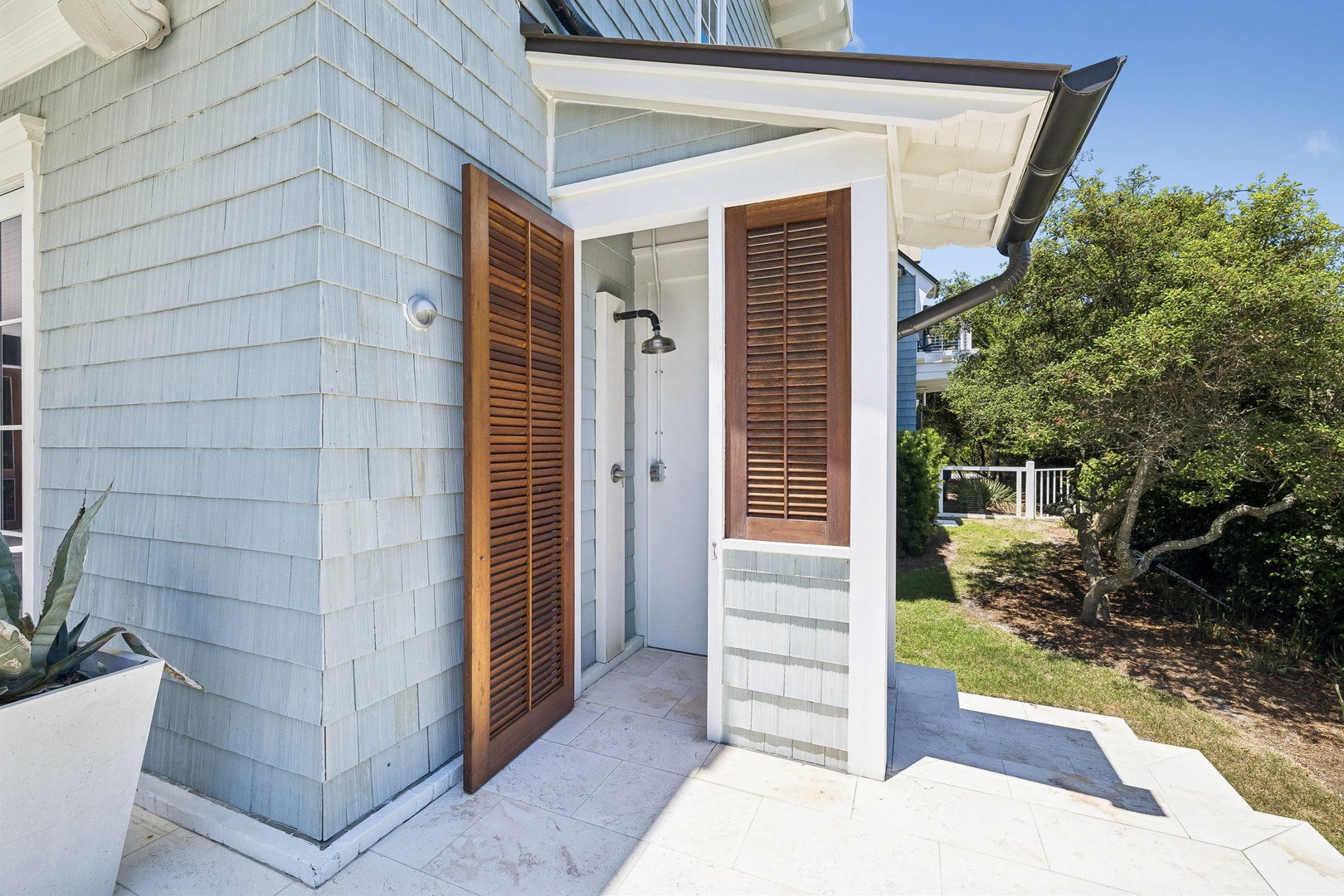 Rinse off after a day at the beach in your private outdoor shower, framed by natural wood shutters and surrounded by coastal landscaping for a seamless indoor-outdoor experience.