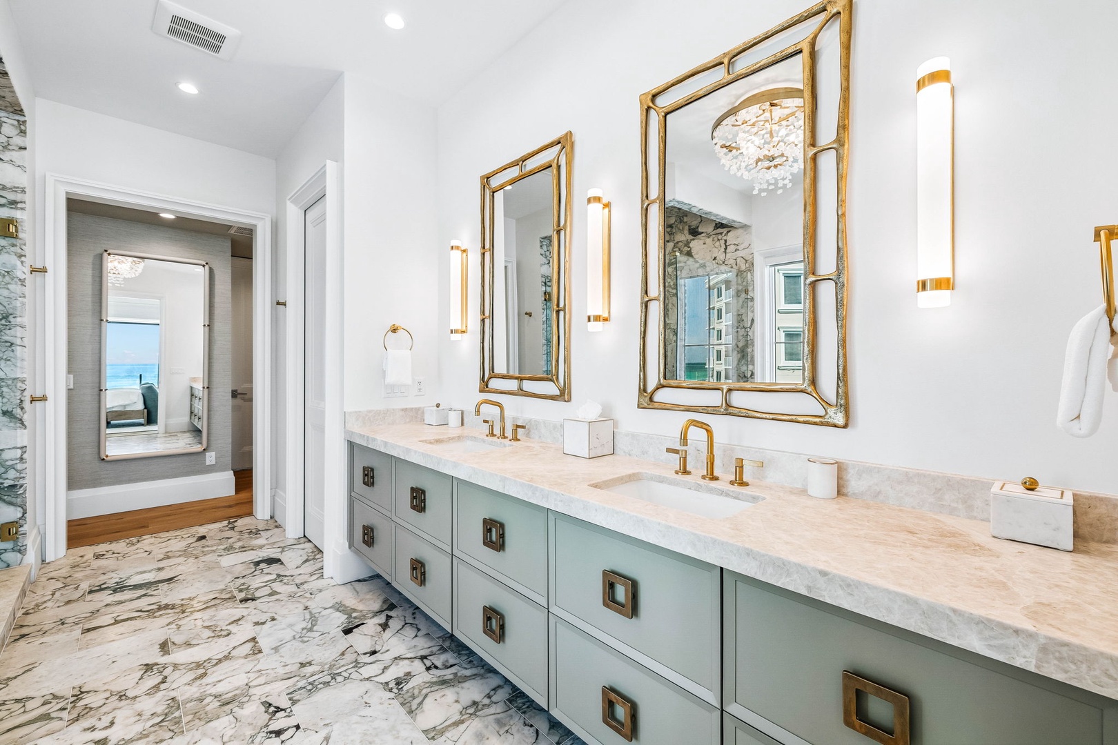 Refresh in your elegant dual-vanity bathroom, where gold accents and marble details create a luxurious coastal retreat—glimpse the sea through the connecting spaces beyond.