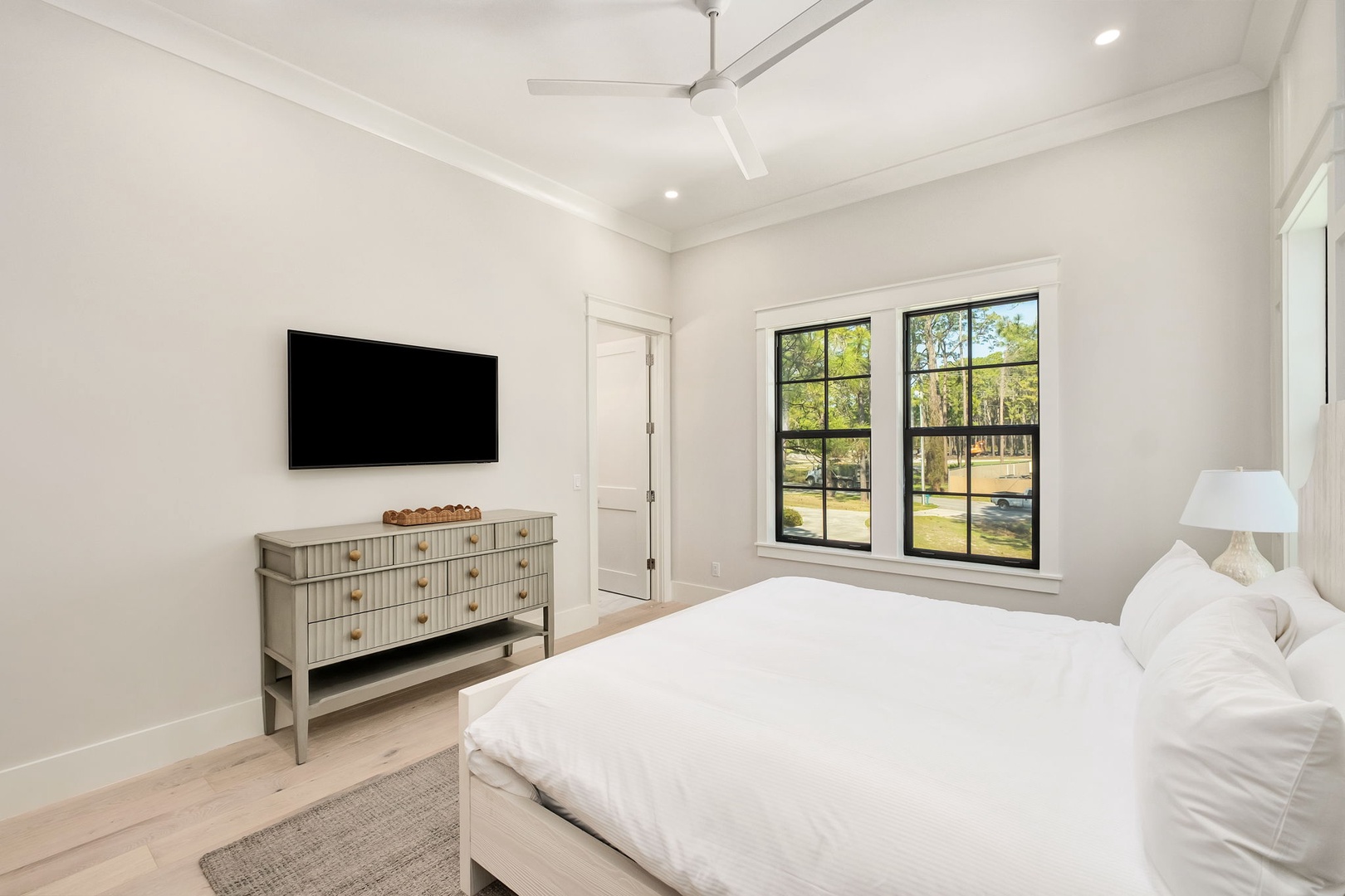 Sink into crisp white linens in your serene bedroom, where natural light streams through large windows and a ceiling fan keeps you cool.