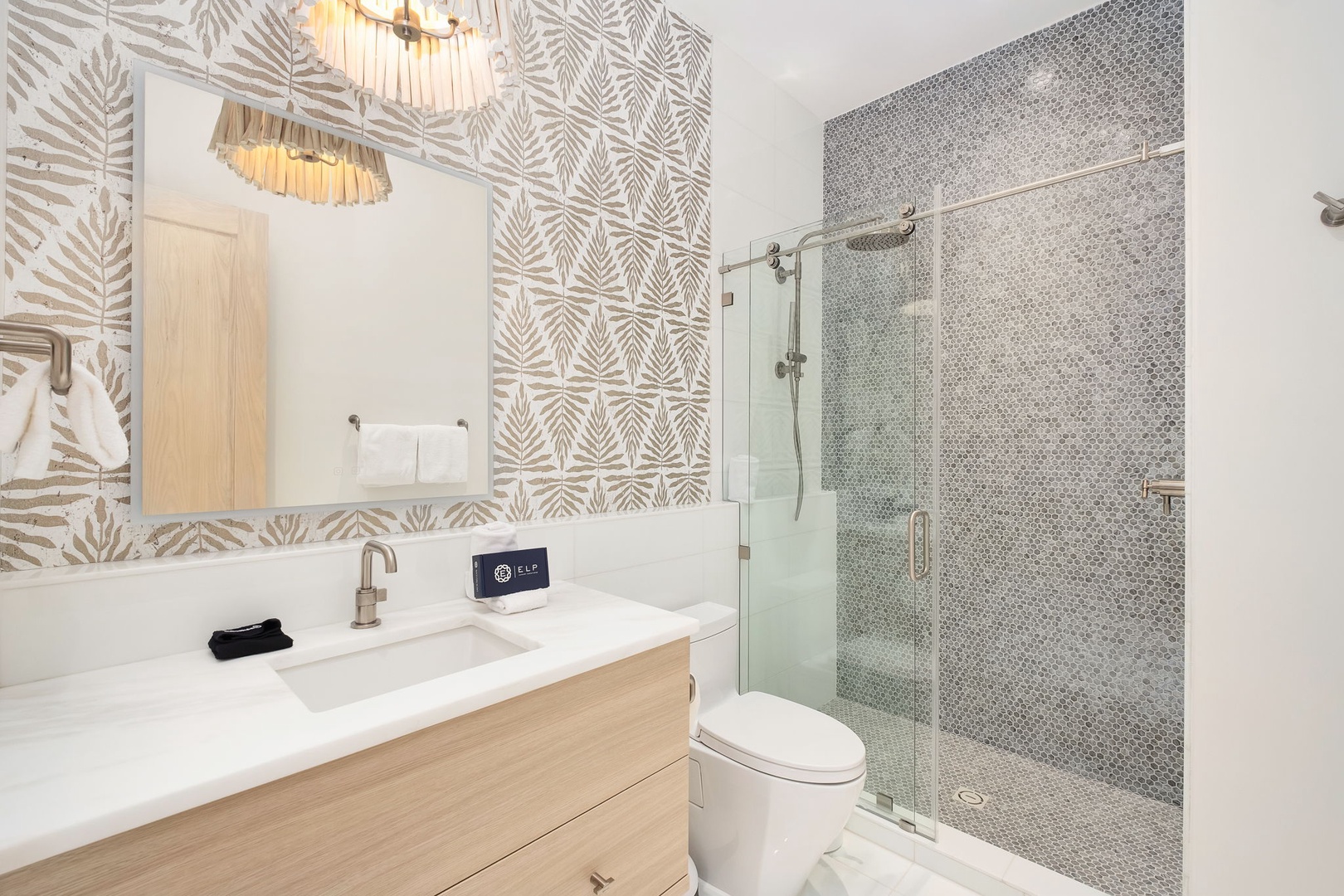 Step into your beautifully designed bathroom, where tropical-inspired wallpaper and elegant mosaic tile create a spa-like retreat for unwinding after your day.