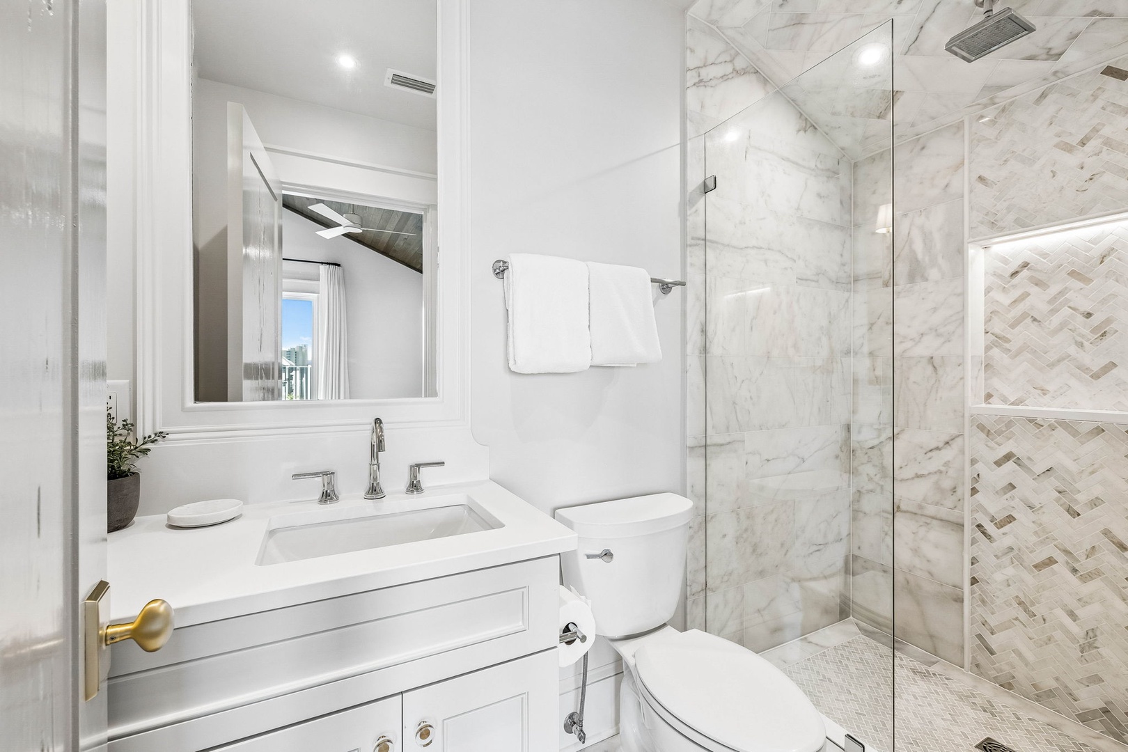 Step into your luxurious marble bathroom featuring a spacious walk-in shower with elegant herringbone tile, pristine white countertops, and designer fixtures throughout.