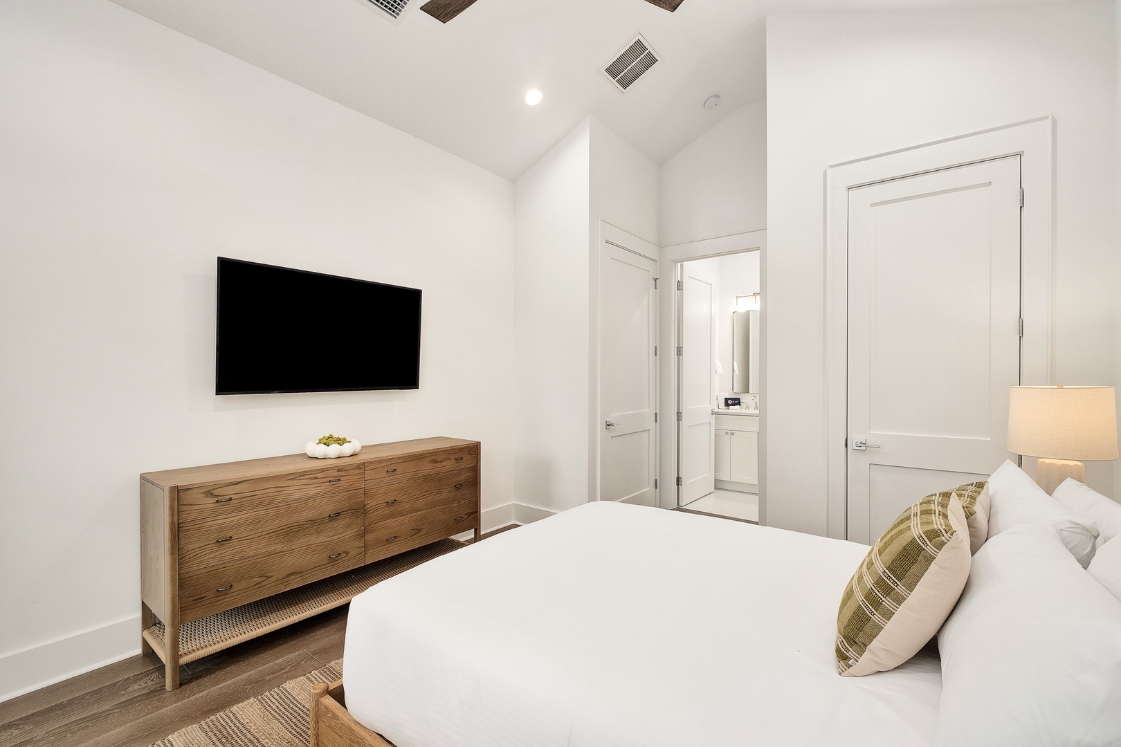 Relax in your pristine bedroom with crisp white linens, modern entertainment, and stylish wood furnishings creating the perfect retreat.