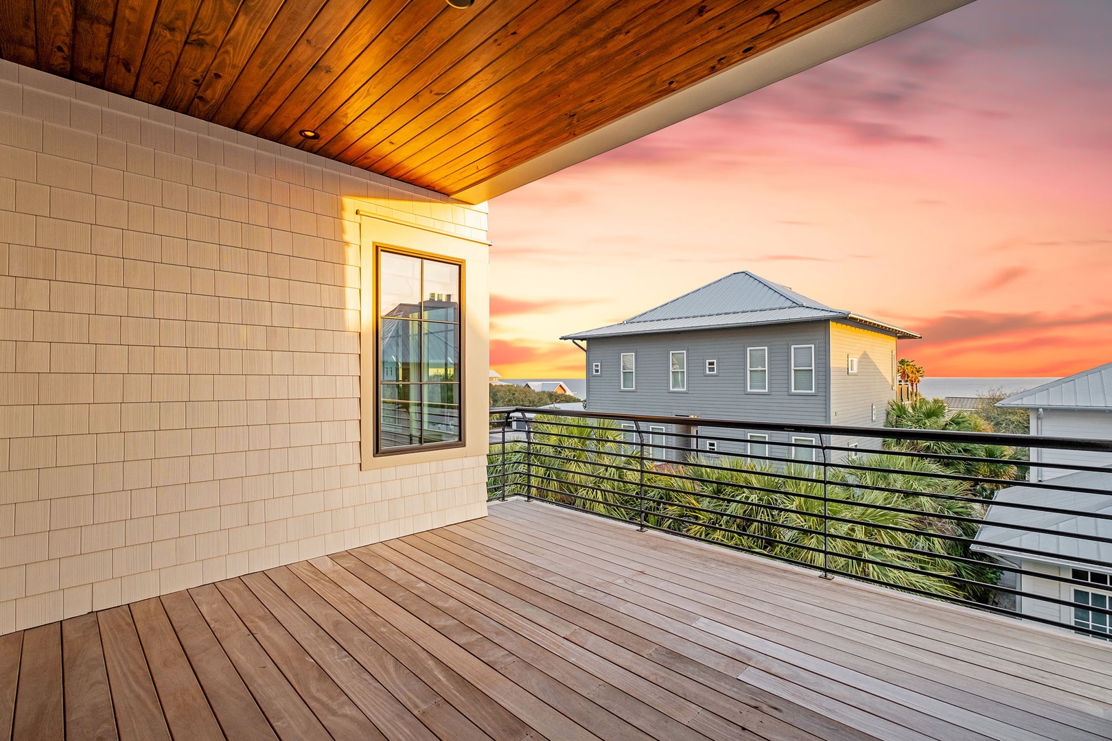 Stunning covered terrace showcases breathtaking sunset views over the neighborhood, featuring warm wood ceiling and sleek railings for your evening relaxation.