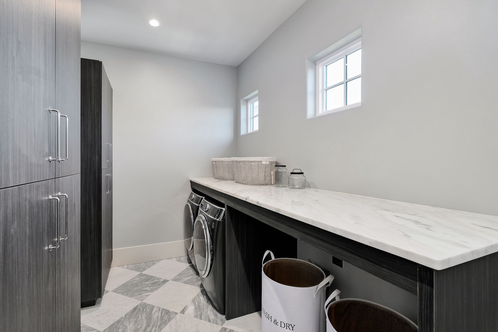 Your pristine laundry room combines style with function, featuring sleek dark cabinetry and marble countertops for easy sorting.