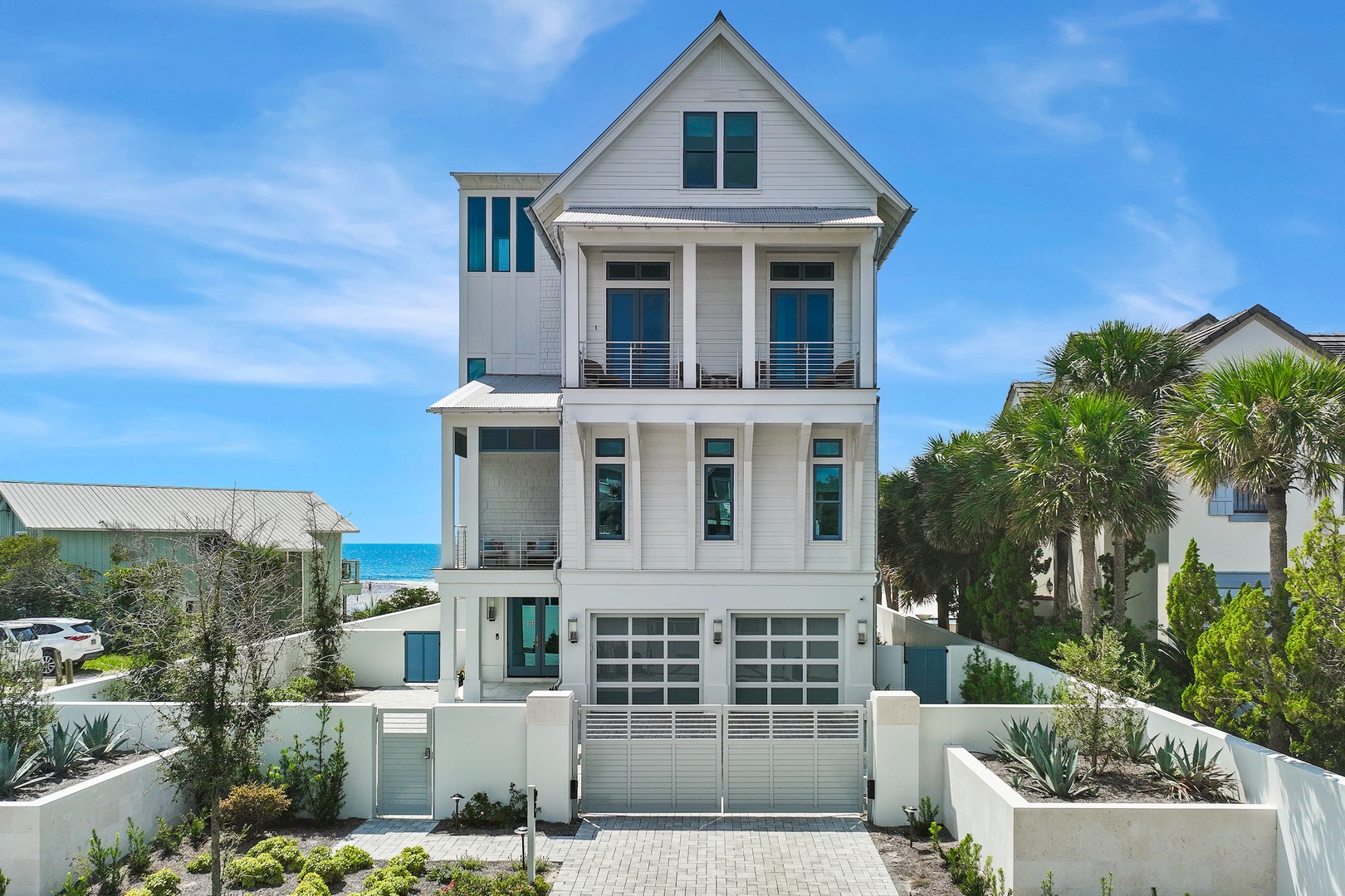 Modern three-story coastal property with a white facade and multiple balconies situated in a palm-tree-lined neighborhood near the beach.
