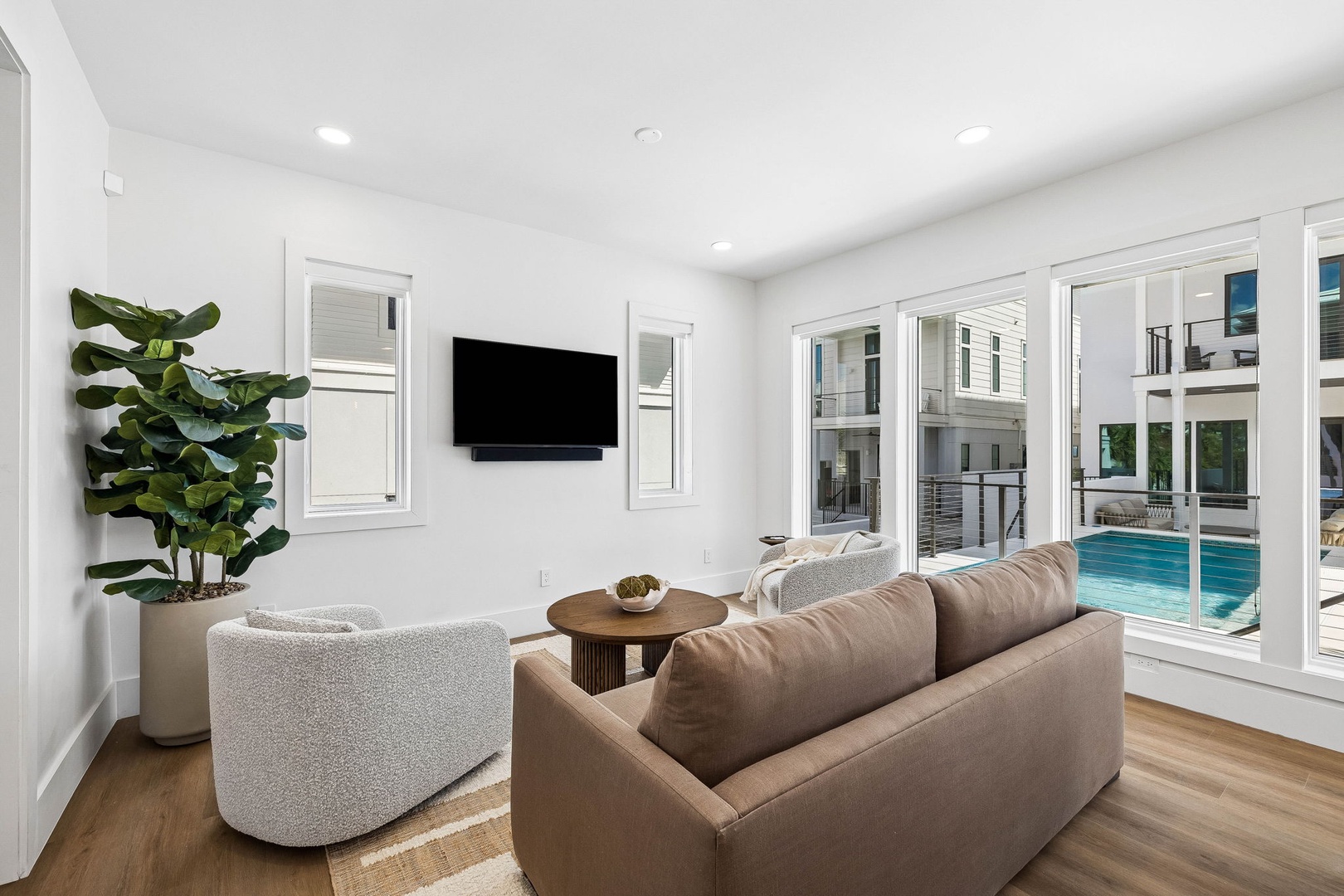 Unwind in your bright, airy living room with sleek furniture and large windows framing the inviting pool just steps away—your perfect spot to relax after a day of exploring.