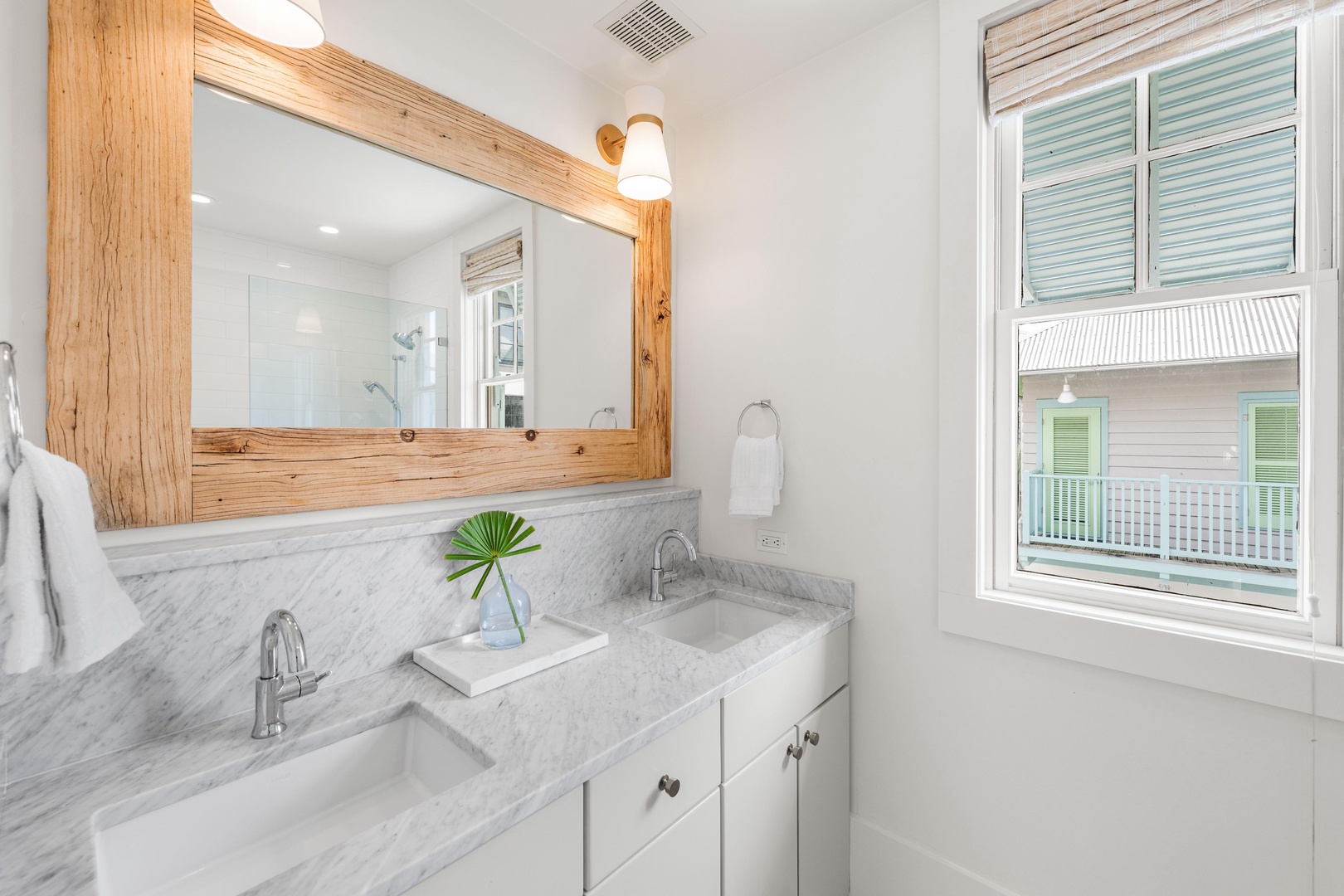 Refresh yourself in this bright bathroom featuring marble countertops, warm wood accents, and natural light streaming through coastal windows.