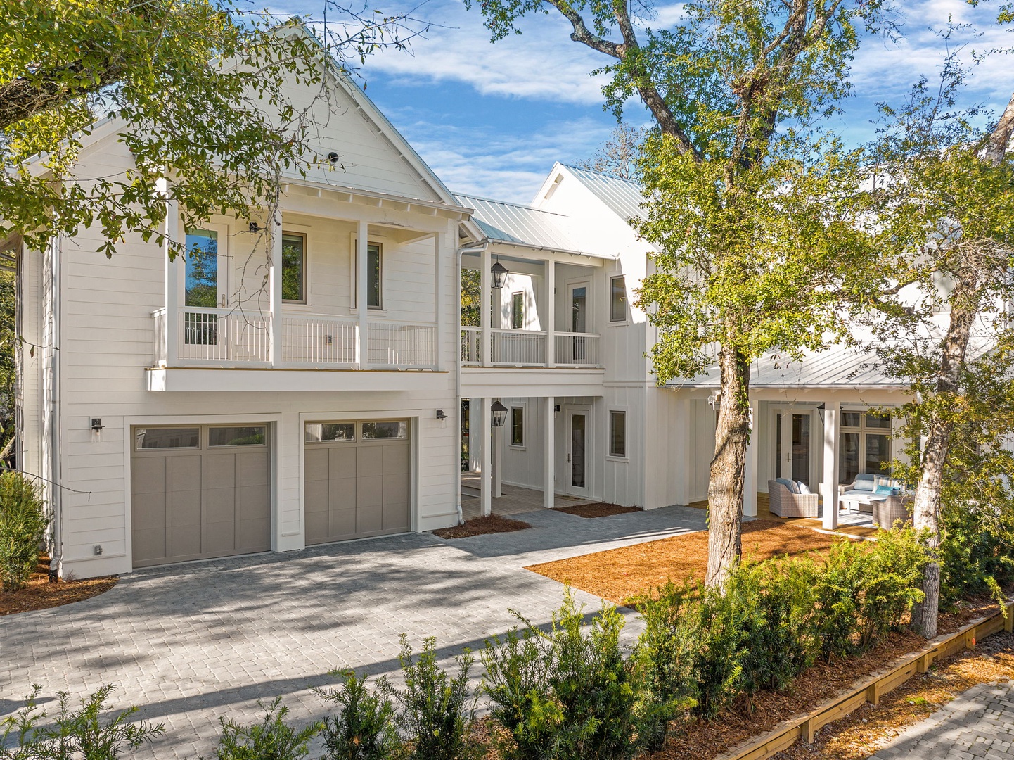 A stunning modern farmhouse with white siding and metal roofing surrounded by mature trees and manicured landscaping.