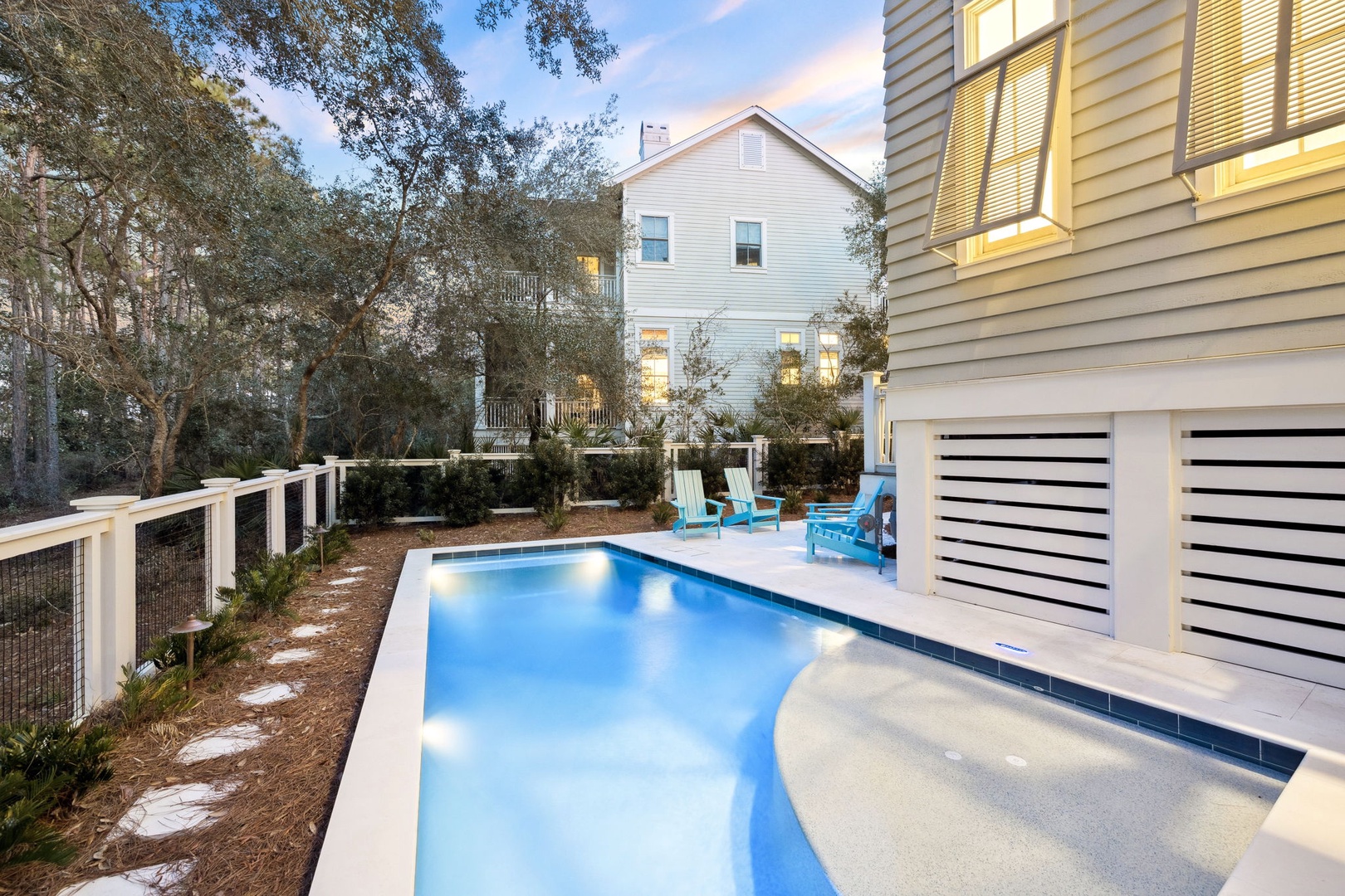 Sparkling private pool awaits in your peaceful backyard oasis, surrounded by coastal charm and turquoise chairs for sunset relaxation.