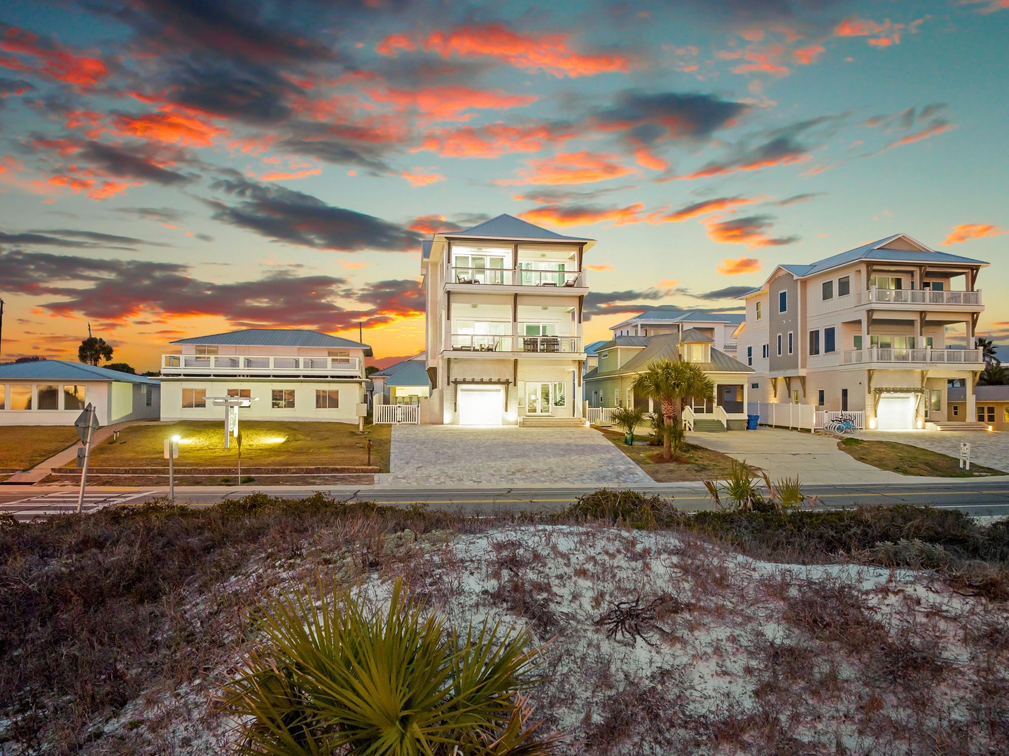 A stunning beachfront neighborhood showcases modern coastal homes beneath a vibrant sunset sky painted in brilliant orange and coral hues.