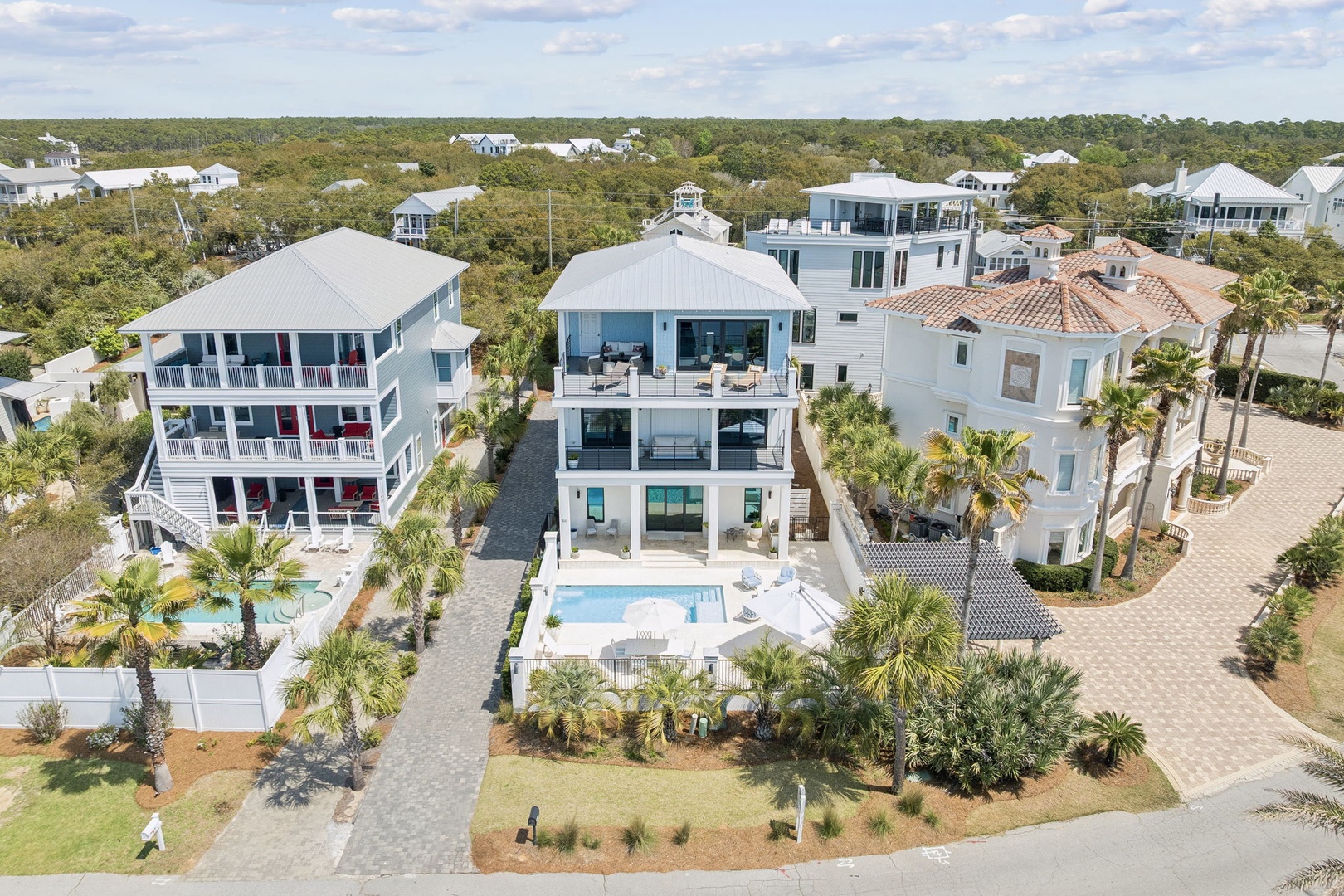 Stunning beachfront estate featuring multiple luxurious homes with pools, surrounded by lush tropical landscaping and neighboring properties in an exclusive coastal community.