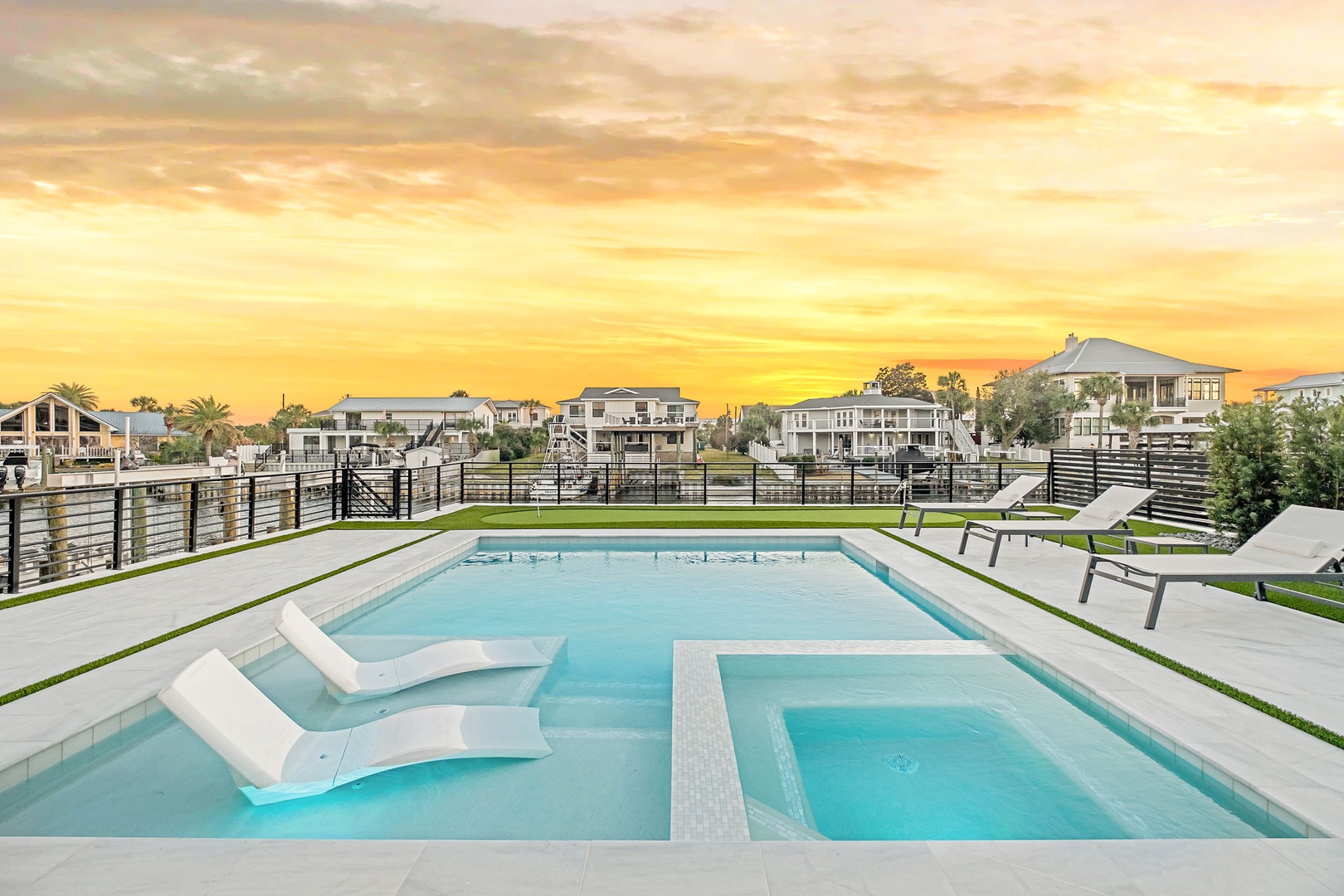 Modern pool area with built-in loungers and hot tub overlooking waterfront neighborhood at golden hour.