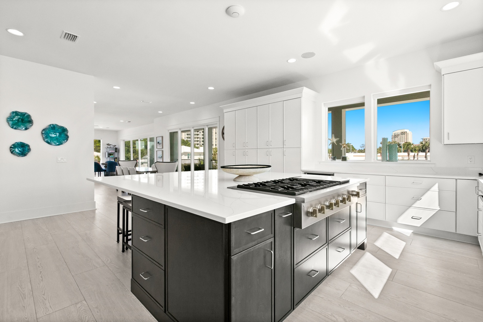 Gourmet kitchen with sleek white cabinetry, island with gas range, and gleaming countertops. Natural light floods the space, creating a bright, inviting area perfect for cooking and gathering.