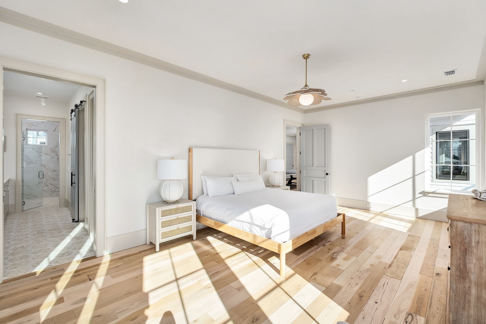 Step into your serene master suite where morning light dances across warm hardwood floors and crisp white linens invite peaceful rest.