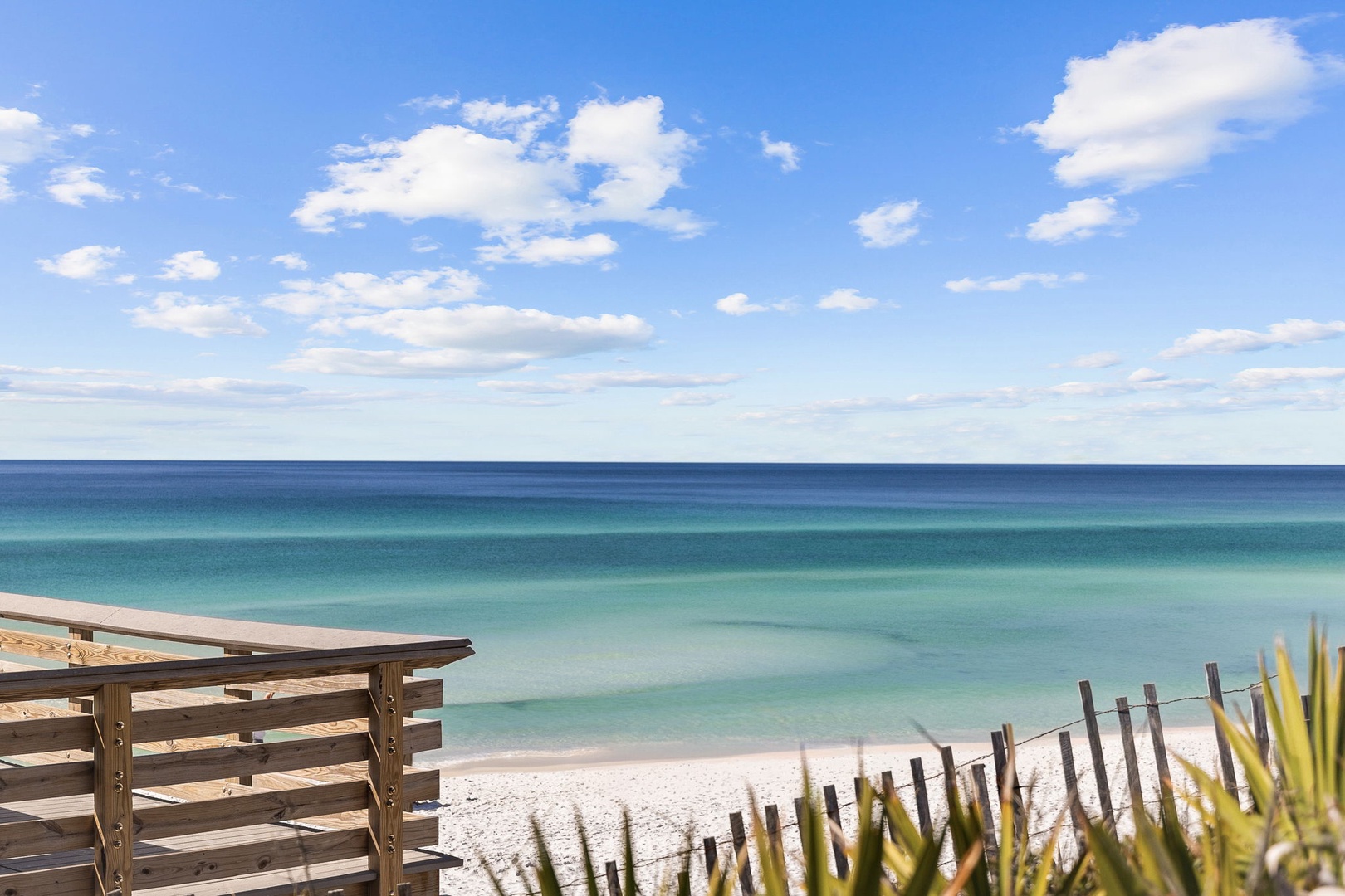 Pristine white sand beach meets crystal-clear turquoise waters under a brilliant blue sky dotted with fluffy white clouds.