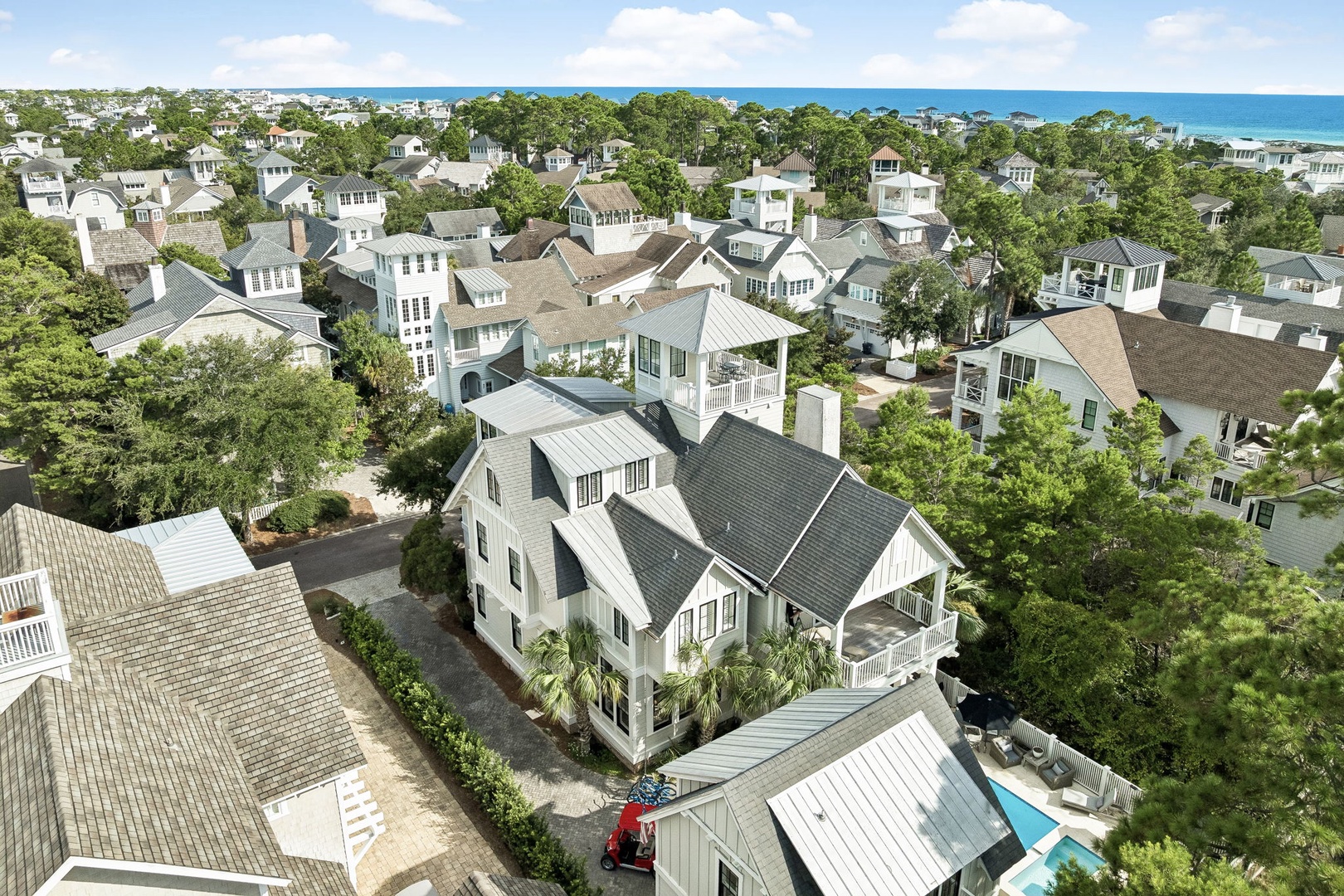 Aerial view of a charming coastal neighborhood nestled among lush greenery, with the Gulf of Mexico visible on the horizon.