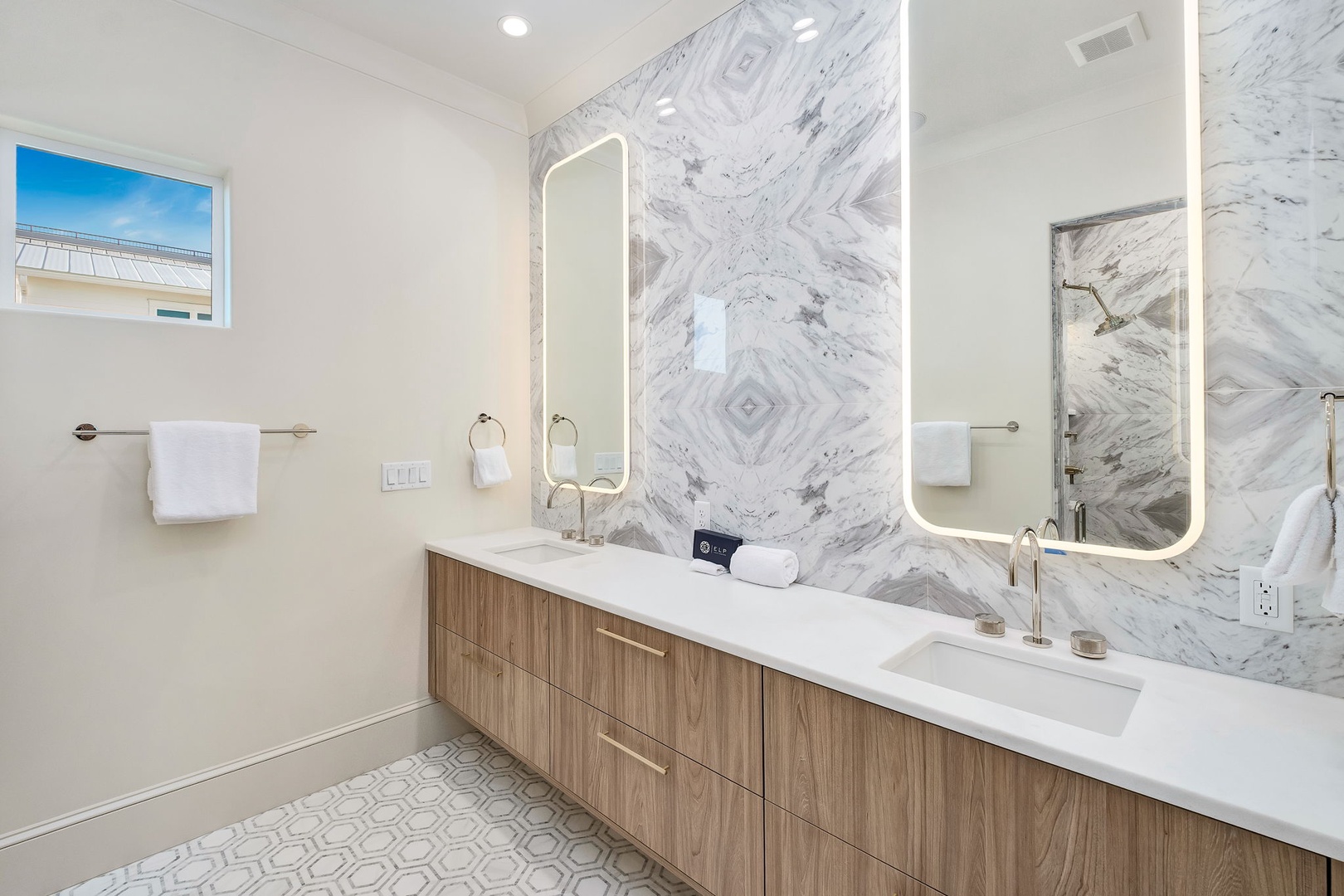 Freshen up in this bright, modern bathroom featuring dual sinks, elegant marble accents, and a spacious glass-enclosed shower that makes your morning routine a breeze.