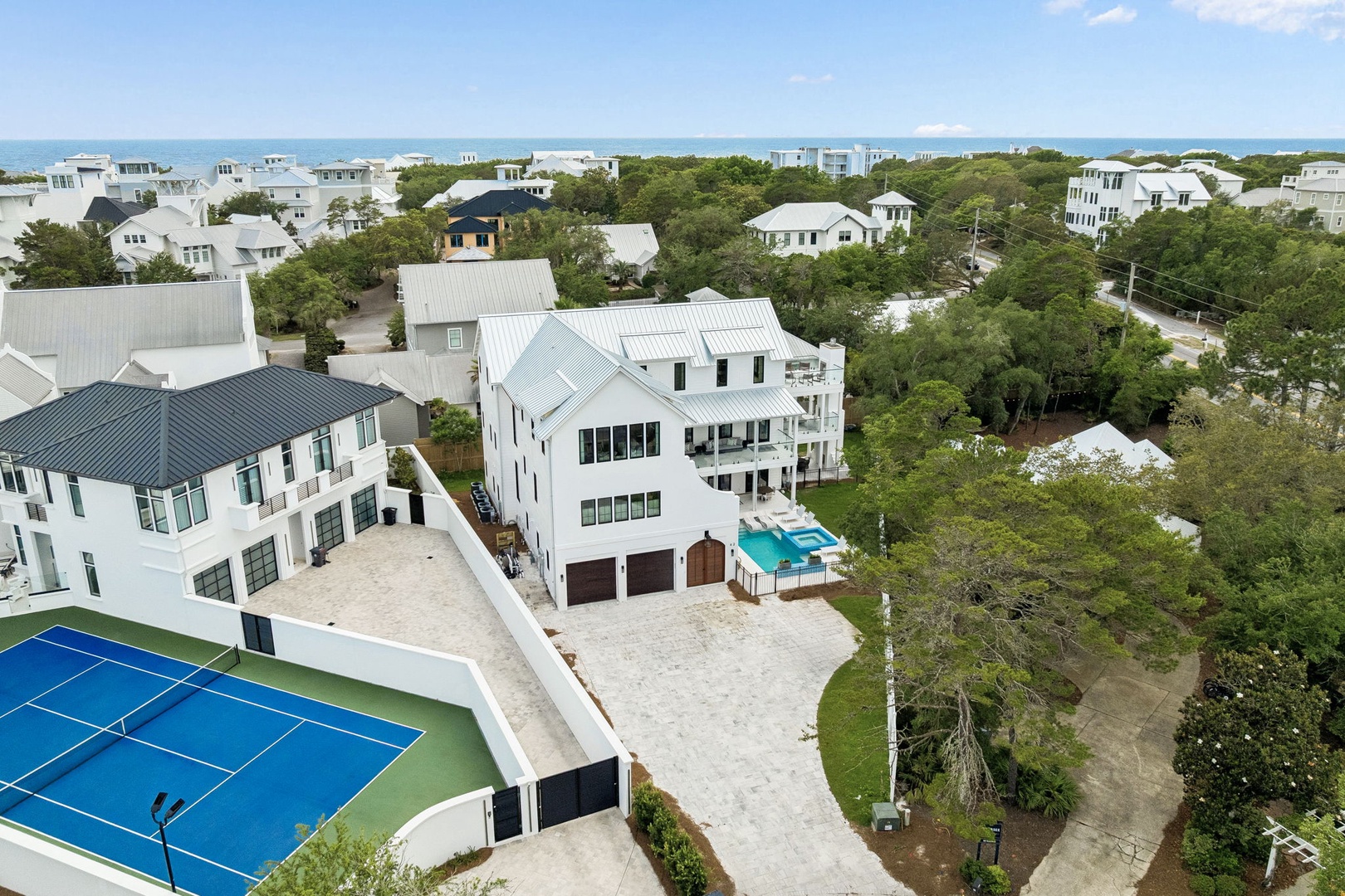 An aerial view captures a luxurious coastal vacation rental property nestled among lush greenery,swimming pool, and spacious outdoor areas—just moments from the pristine ocean shoreline.